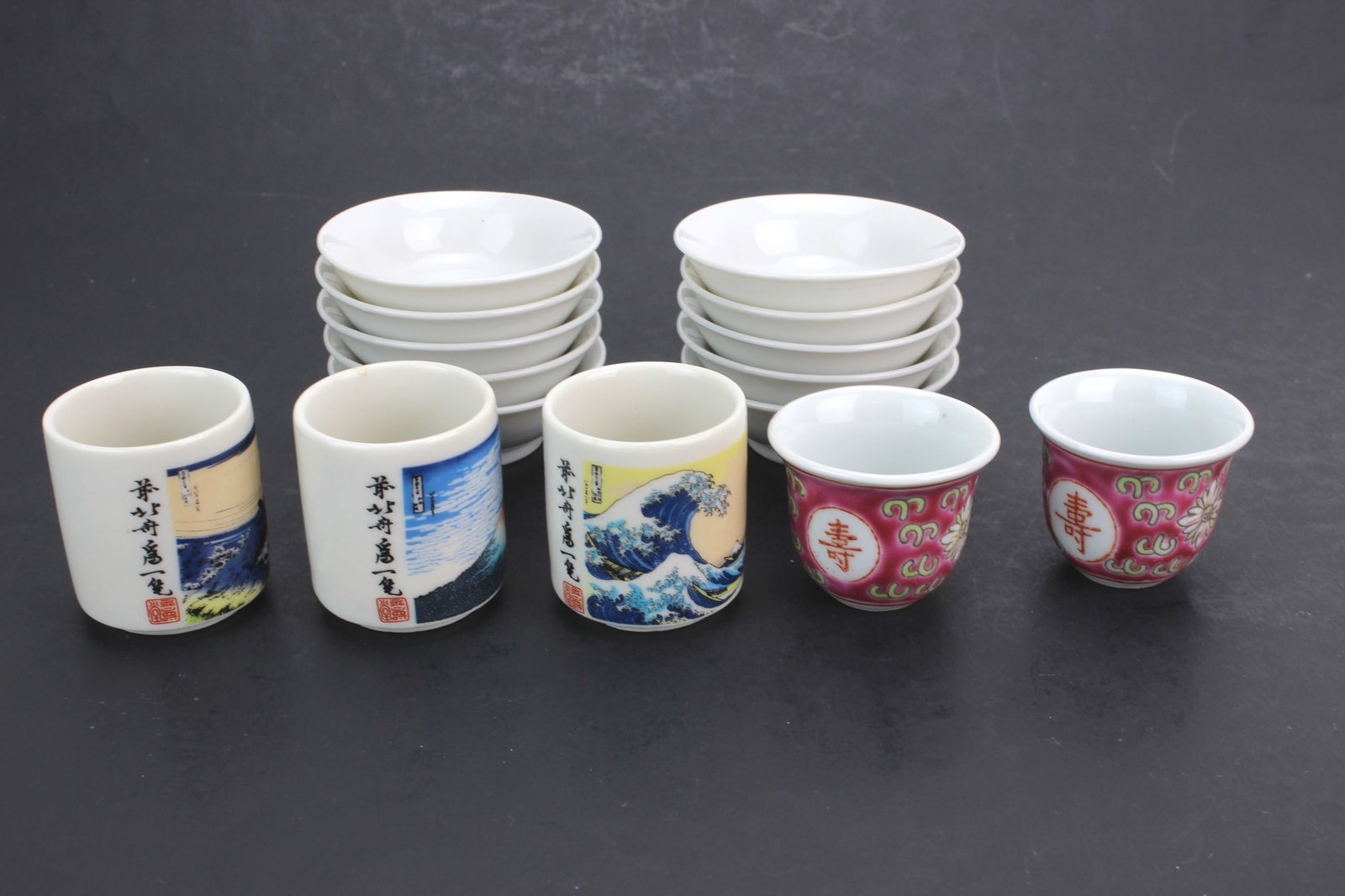 Group of 11 Asian Sake Articles: Collection of 11 Asian porcelain sake articles including 3 decorated sake cups, 2 famille rose style cups, and 6 small sauce bowls. Sake cups measure 1 3/4 in. tall; small sauce bowls measure 2 1/2
