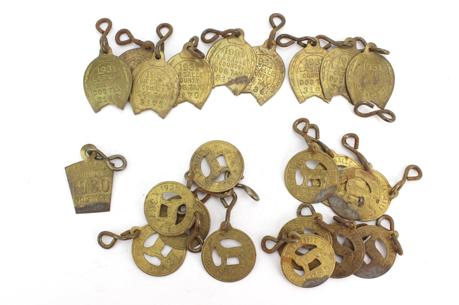 23 LaSalle County Dog Tax Tags: Lot of 23 early LaSalle County, Illinois dog license tax tags including lucky horseshoe and dog motif examples, dated 1928?1931. Each measures approx. 1 1/2 in. (L). Showing oxidation, tarnish,