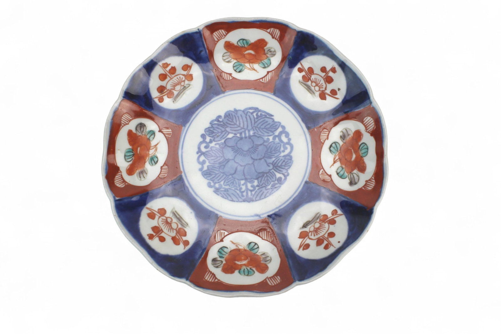 Japanese Imari Porcelain Plate: Japanese Imari porcelain plate with floral and cartouche decoration in blue, red, and green enamels, scalloped rim, and branch motifs on the reverse. Minor rim frits and glaze wear. Size approx. 8
