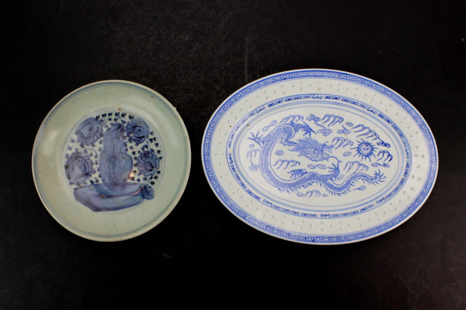 Two Chinese Blue & White Porcelain Dishes: Two Chinese blue-and-white pieces: an old 8 in. dish with floral design showing glaze wear, frits, and age-related flaws; and a 12 in. (L) by 8 3/4 in. (W) rice-grain oval plate with dragon motif,
