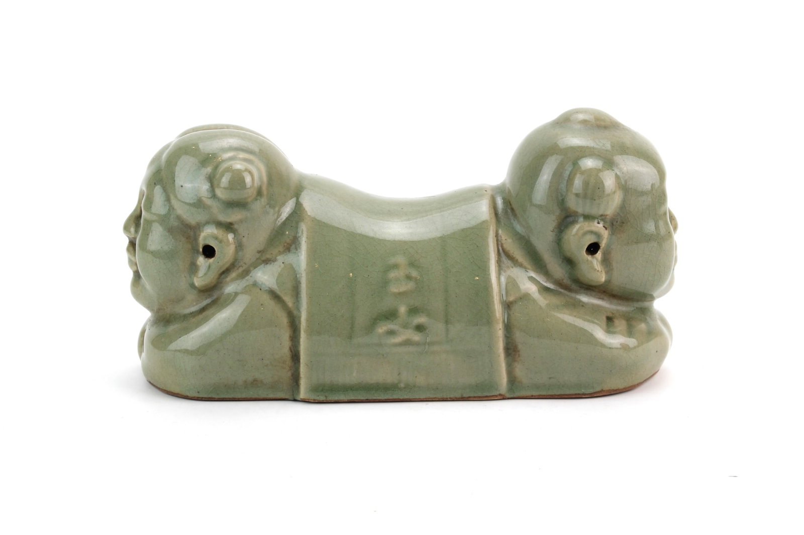 Chinese Celadon Figural Hand Pillow: Chinese celadon-glazed porcelain hand pillow modeled with two reclining child figures joined by a central support, covered in a soft green glaze with fine crackle. Measures 9 1/2 in. (L) x 3 3/4 in. (