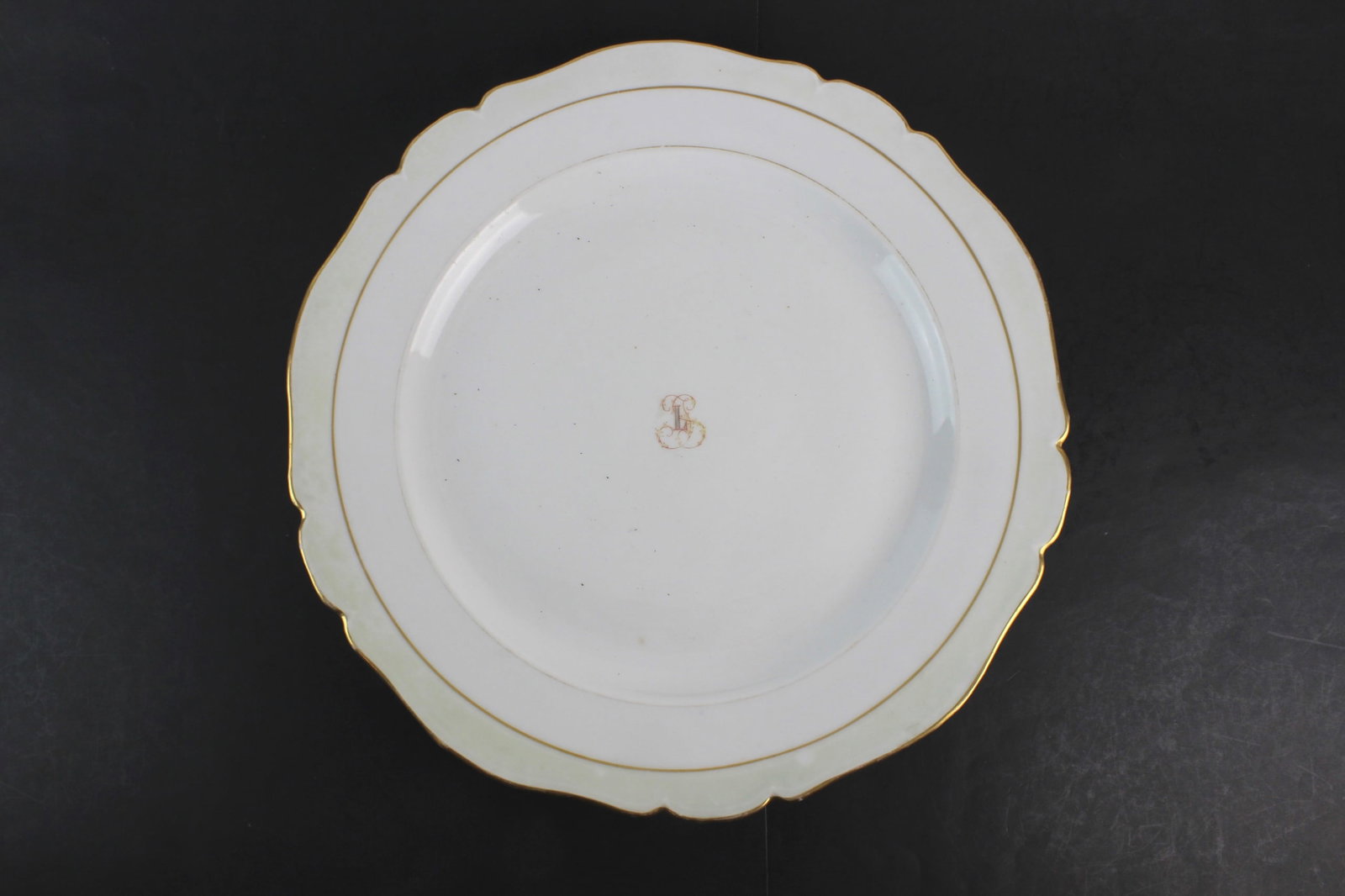 Porcelain Platter w/ Gilt Rim: Porcelain serving platter with scalloped rim and gilt trim, featuring a central monogram decoration.Approx. size: 17 1/2 in. (D) X 2 in. (H). Overall good condition with light wear consistent with
