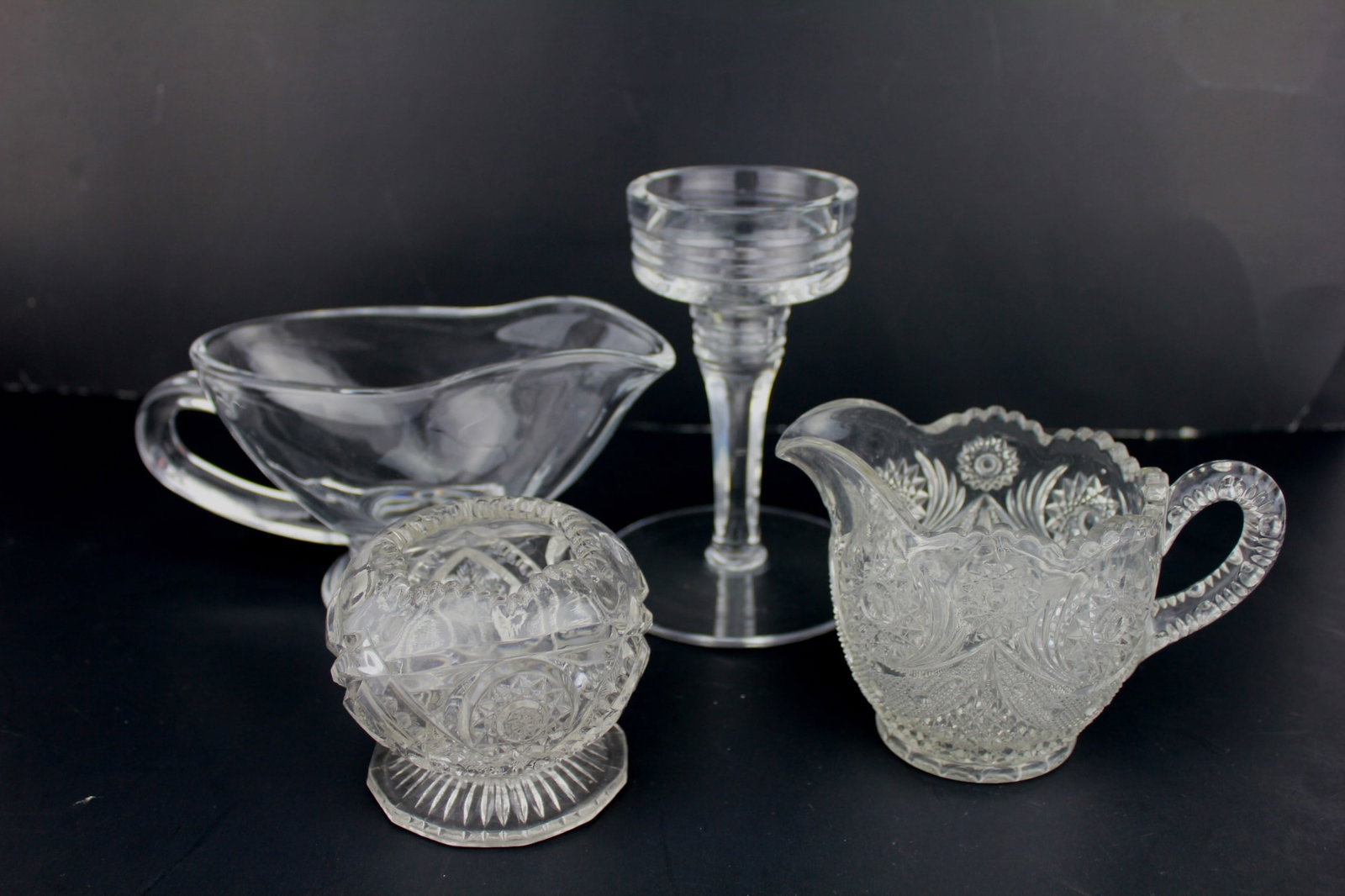 Four Cut Glass Tablewares: A 4-piece antique cut glass tableware set featuring a clear gravy boat (in 7 1/2 in. L), ornate creamer (in 5 1/2 in. L.), decorative sugar bowl (3 in. H.), and a ribbed-rim stemmed glass (in 5 1/2 in