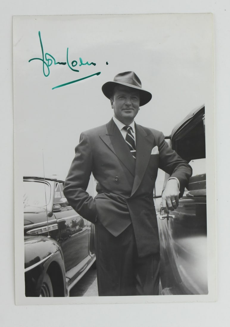 Signed Photograph of John Loder: Vintage black-and-white signed photo of John Loder posing in a double-breasted suit and fedora beside a classic car. Signature in green ink at top left. Light handling wear and faint surface marks;