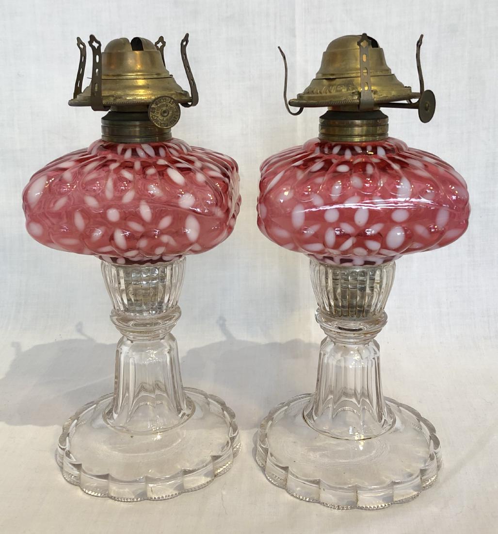 Pair Antique Oil Lamps with Cranberry Glass Fonts: Lovely matched pair of antique lamps with cranberry and white fonts out of a rural Maine estate collection of early lighting. Burners are marked Banner. Mercury glass in center under font. 9"H