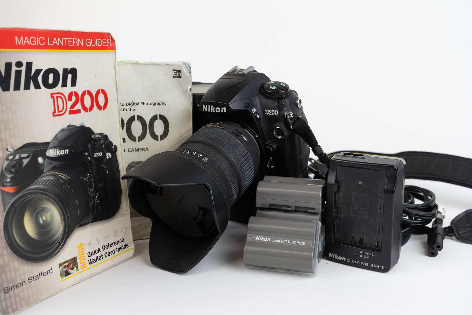 Nikon D200 with Batteries: A Nikon D200 digital camera with a Sigma DC 17–70mm F2.8–4.5 lens. Has lens hood and rear display protector. Comes with manuals, four batteries, and a battery charger. H6" W6" D7" (Dimensions of l