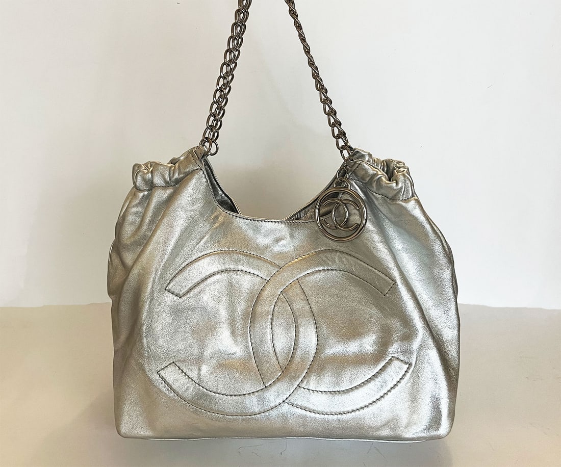 CHANEL BABY COCO CABAS TOTE: CHANEL BABY COCO CABAS TOTE SILVER This is an Pre-owned CHANEL Coco Cabas in Silver. The bag features chain link cinch cord top handles and a hanging Chanel CC medallion. The top opens with magnets to