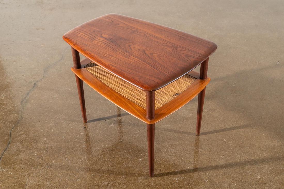 Peter Hvidt Teak and Cane Modern End Table: A pair of teak Danish Modern end tables designed by Peter Hvidt for France and Son. Crafted in solid teak with a woven cane magazine shelf under tabletop. Conical legs and woven wicker detail. CREATOR