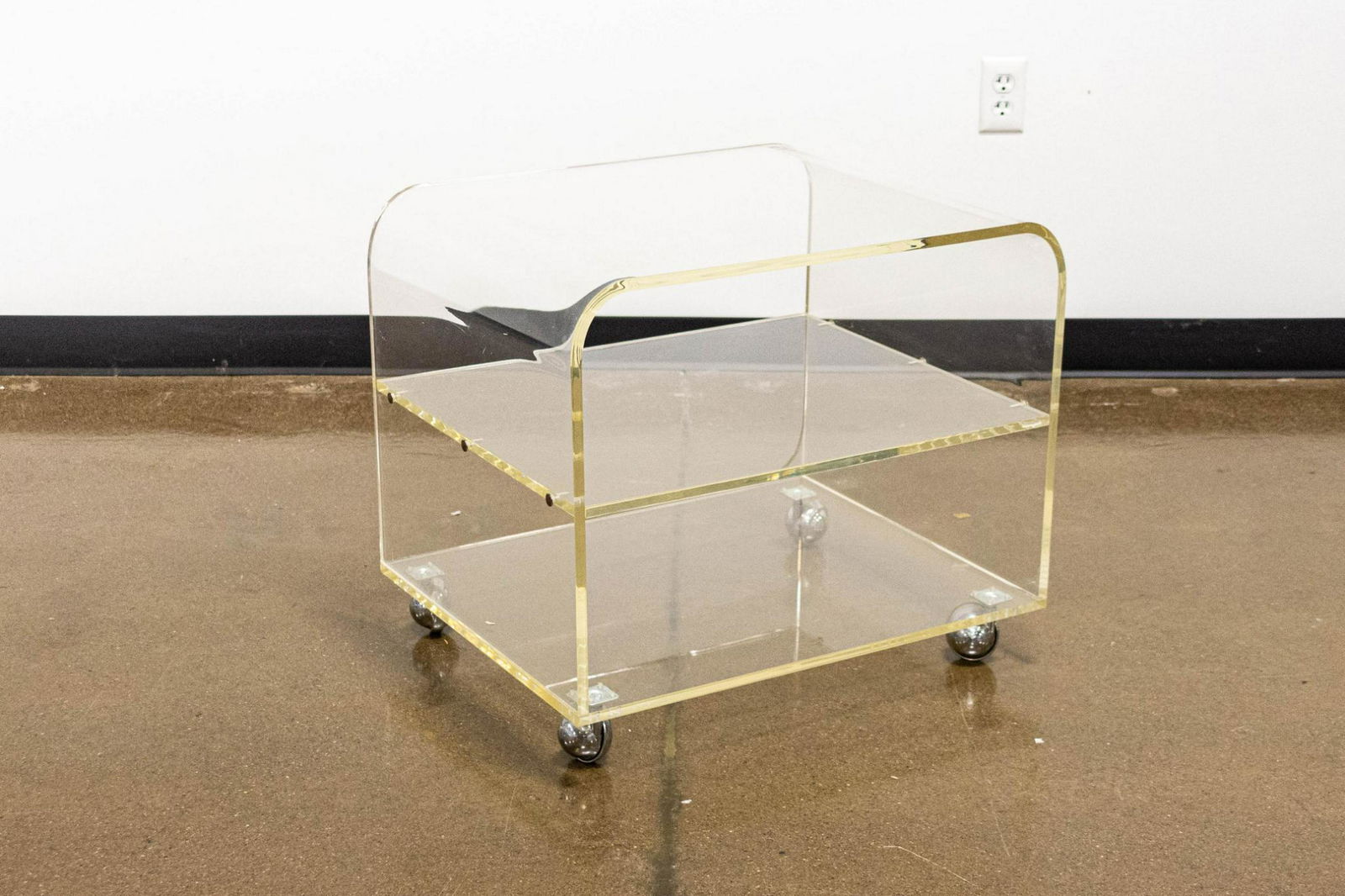 Clear Acrylic Two-Tiered Side Table on Chrome Coasters: Two-tiered clear acrylic side table on chrome coaster wheels. Says Shepard on the coasters. ARTIST: Unknown CONDITION: Very good, shows signs of normal use DIMENSIONS: 21" x 24"