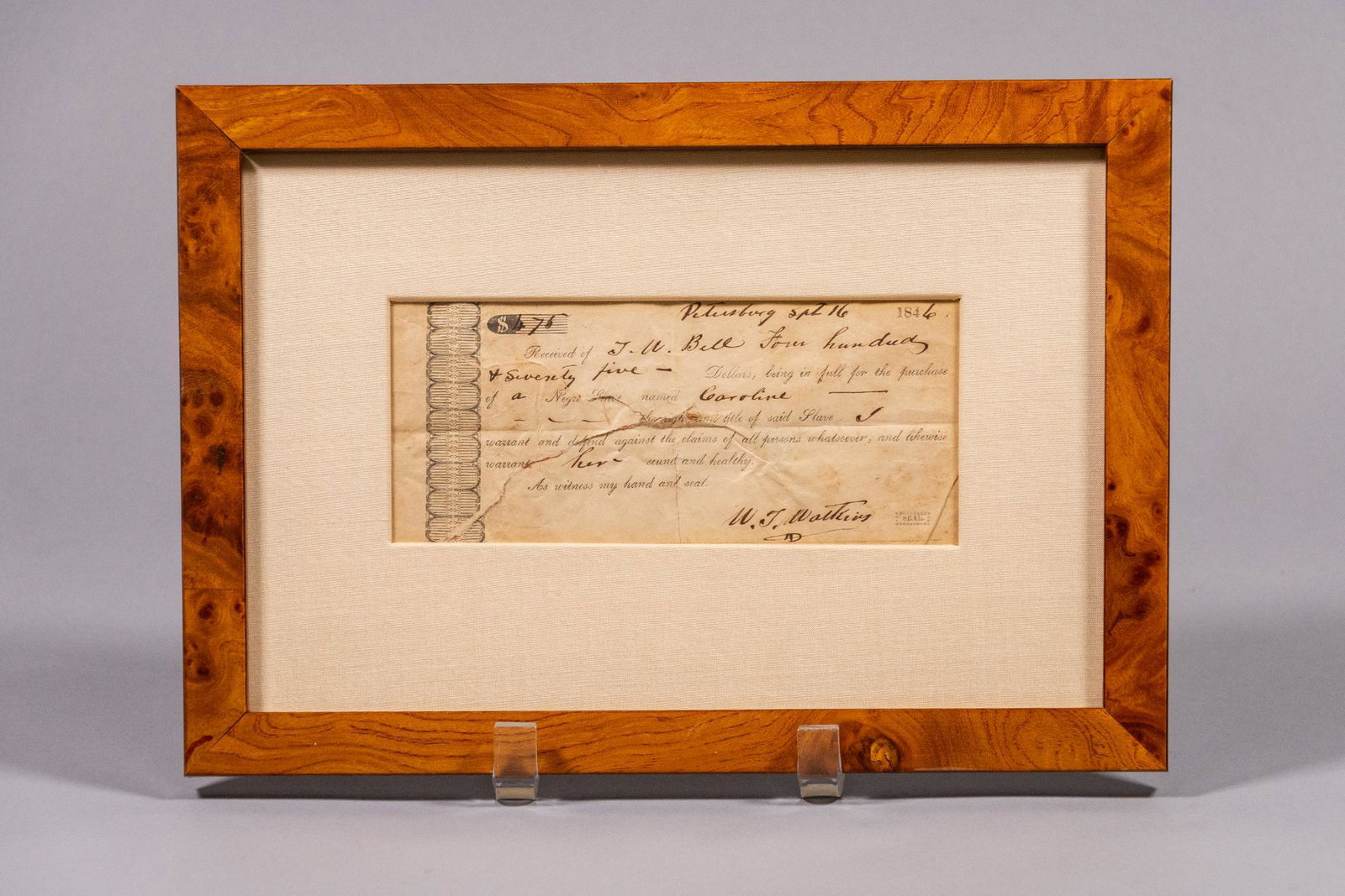 Framed Historical Slave Purchase Receipt, 1846: This is a receipt of purchase for a slave, a woman named Caroline, dated September 16, 1846 in Petersburg, and signed by W.J. Watkins. This document is in a light brown wood grain frame and matted wit
