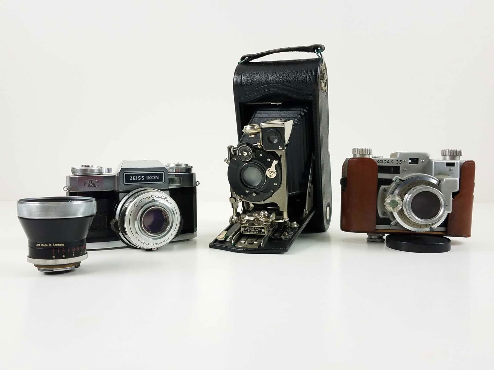 Three (3) Vintage Cameras and One (1) Lens: This is a lot of three (3) vintage cameras. Includes: One (1) 35mm SLR German-made Zeiss Ikon Contaflex with brown carrying case and strap. CONDITION: Very good. The case has some scuffs and rusty bit