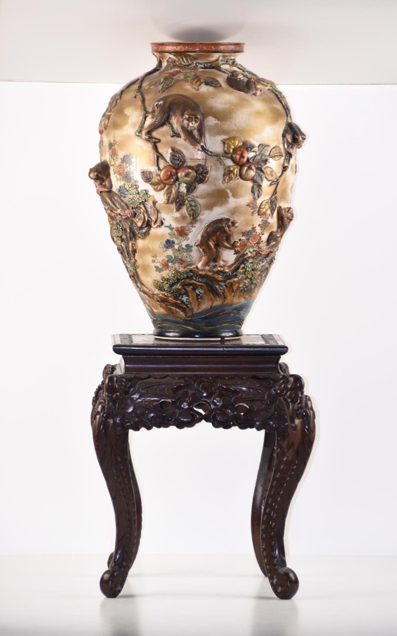 Ceramic Asian Monkey Vase with Wood Stand: Asian-style ceramic vase with a 3-D monkey scene. Signed on the bottom. This includes a wood stand with ornately carved legs. MEASUREMENTS: The vase: 19" x approx. 13". The opening is 6" in diameter. 