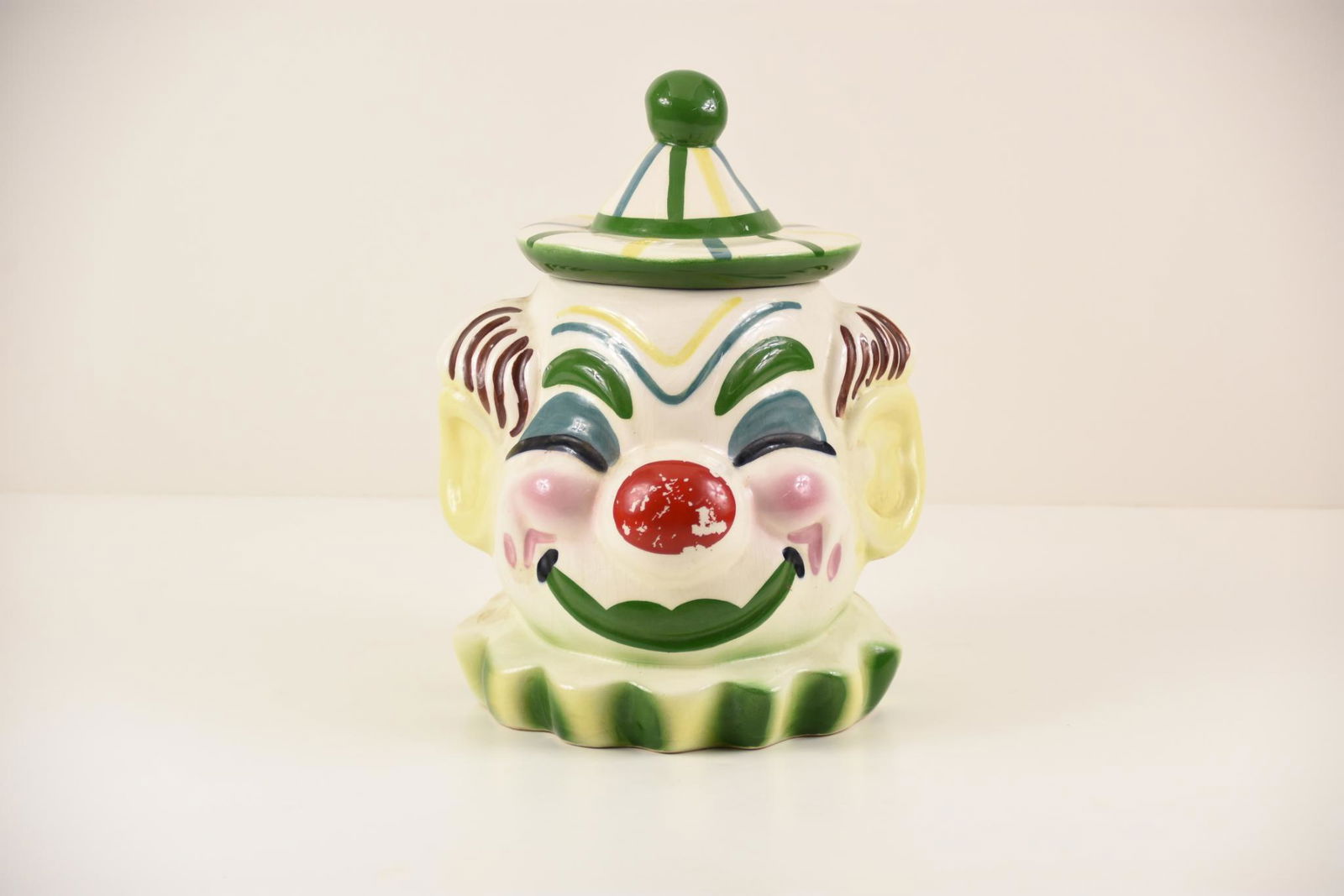 Vintage Ceramic Clown Cookie Jar: Vintage ceramic clown cookie jar with green details. MEASUREMENTS: stands approx. 11.5" x 11". measures 24" around. CONDITION: Good. Glaze is cracked and the paint is coming off on the nose.
