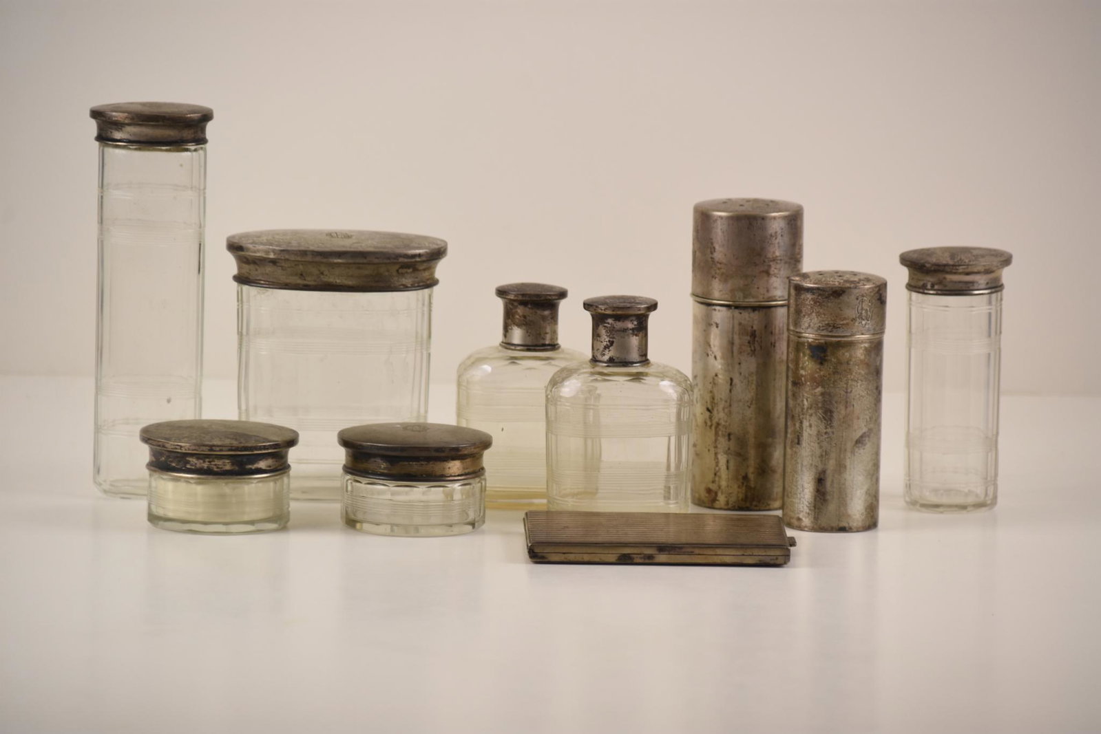 Antique Silver Cosmetics Bottles, Jars, and a Cigarette: This is a lot of cosmetic bottles, jars, and a cigarette case. Includes: Two (2) glass perfume bottles with silver caps with a monogram. MEASUREMENTS: 3.75" x 2.75" x 1.5" CONDITION: Good. One (1) cyl