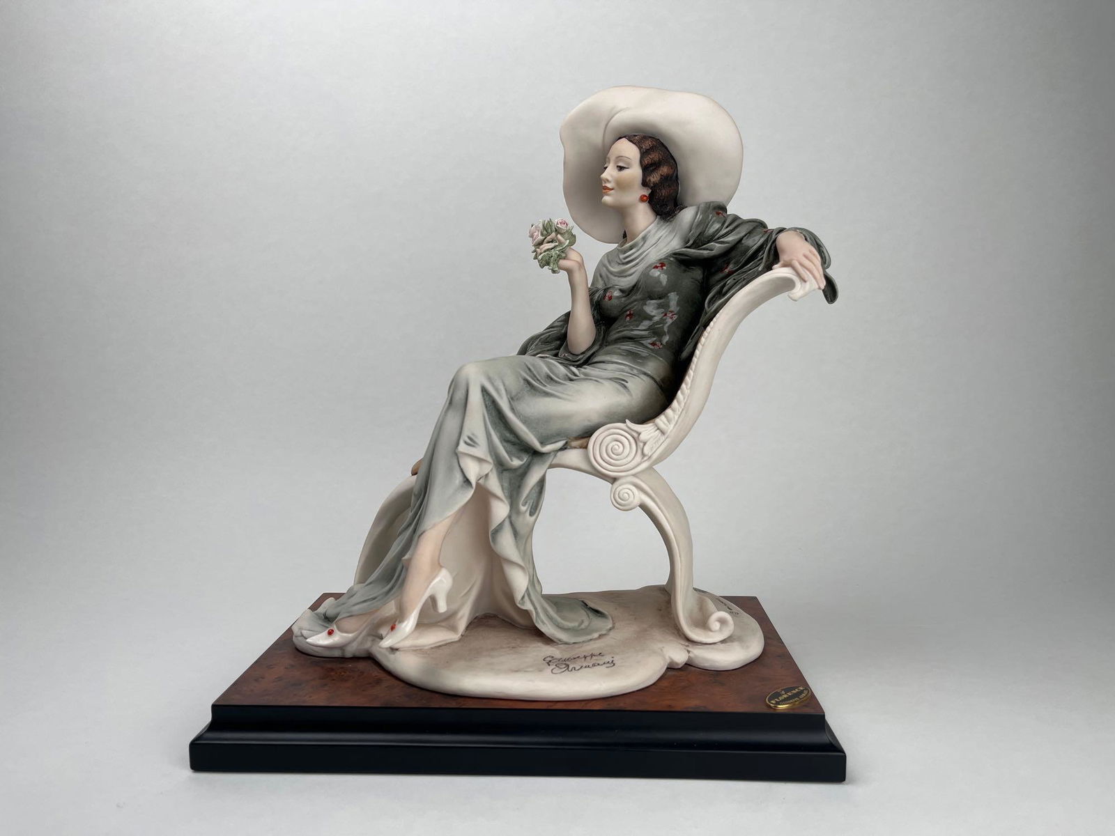 Limited Edition Giuseppe Armani â€œAt Easeâ€ 634-C: Limited-edition Guiseppe Armani porcelain statue. Titled "At Ease", it features a woman in a hat lounging on a chair. This limited-edition piece is numbered 1083/5000. Provenance: The piece c
