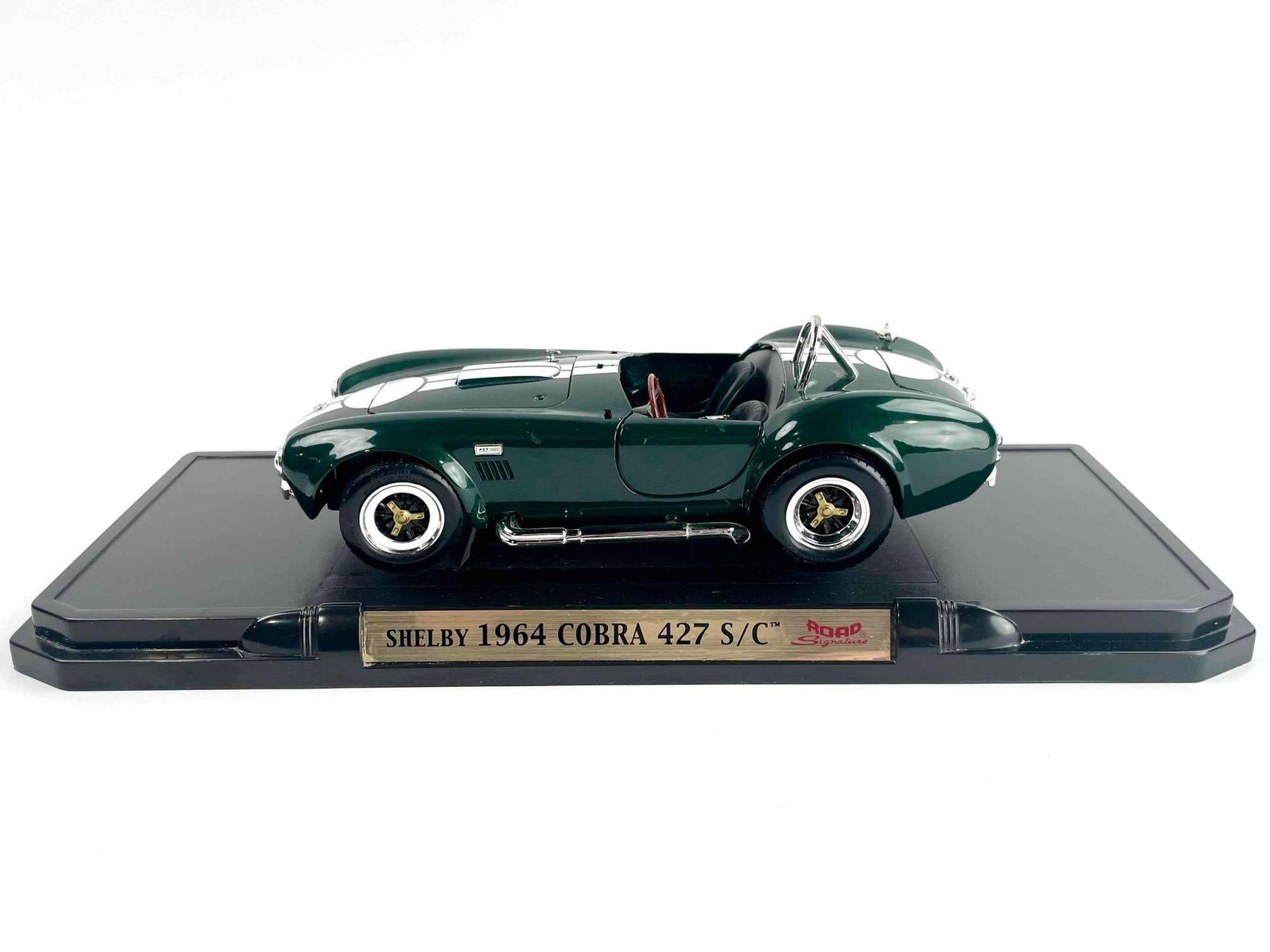 1964 Shelby Cobra 427 Model Car: 1964 Shelby Cobra 427 model car in green with white stripes. Car features opening doors, hood, and trunk. Base is not removable. Car is in fair condition and missing the windshield, as well as the dri