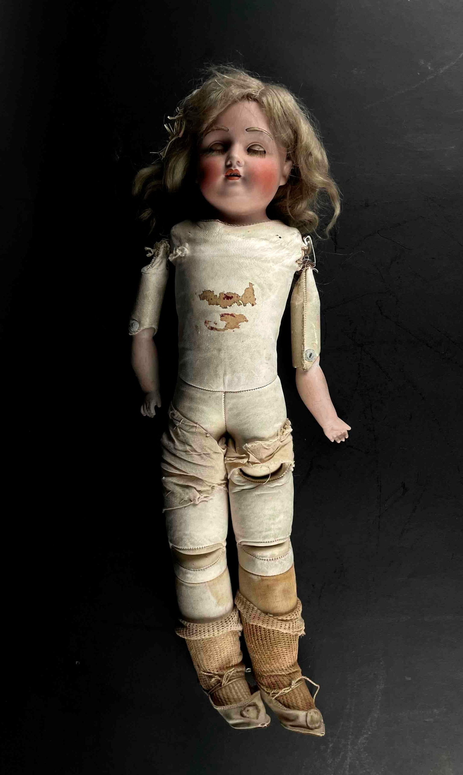 Antique German Porcelain Doll: Antique German porcelain doll with blonde wig, blue glass eyes, and leather body stuffed with saw dust. Doll wears a pair of nude ballet shoes with leg warmers. Doll face is in good condition with ros