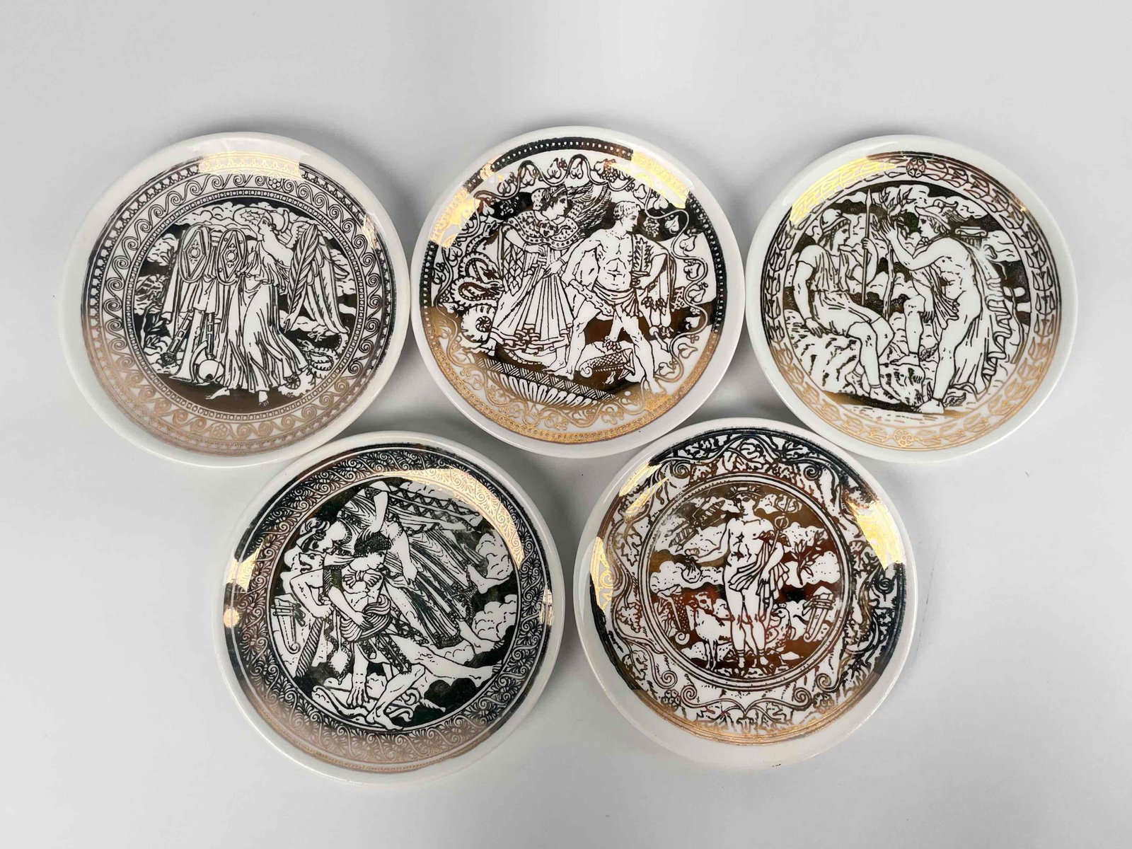 5 Piero Fornasetti 'Mitologia' Coasters: Five Piero Fornasetti 'Mitologia' Coasters. Italian white porcelain with gilt gold mythological scenes. Hallmark is present on back of each dish. In good condition with light surface wear such as fadi