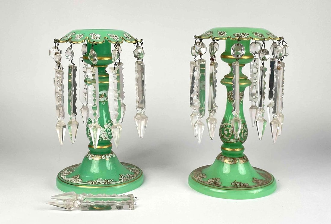 Pair of Green Bohemian Mantle Lusters: Pair of bohemian mantle lusters with dangling crystal prisms. Green in color with hand painted white and gilt floral detailing. One mantle luster is missing hooks for hanging two crystals. Crystals ar