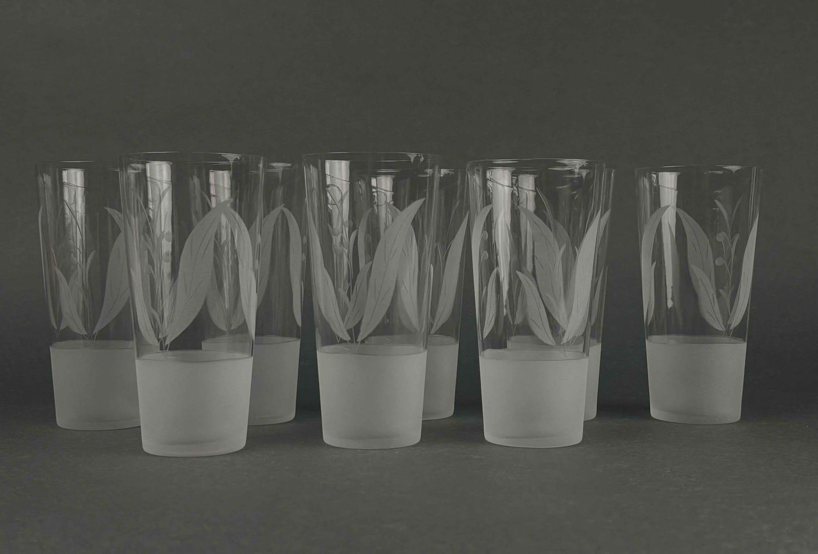 Art Deco Etched Glassware (circa 1950s): Set of 8 etched glass highballs, circa 1950s. Botanical motif with concentric bands. Glasses are in excellent vintage condition. One glass has a chipped rim as pictured. Please see photos for addition