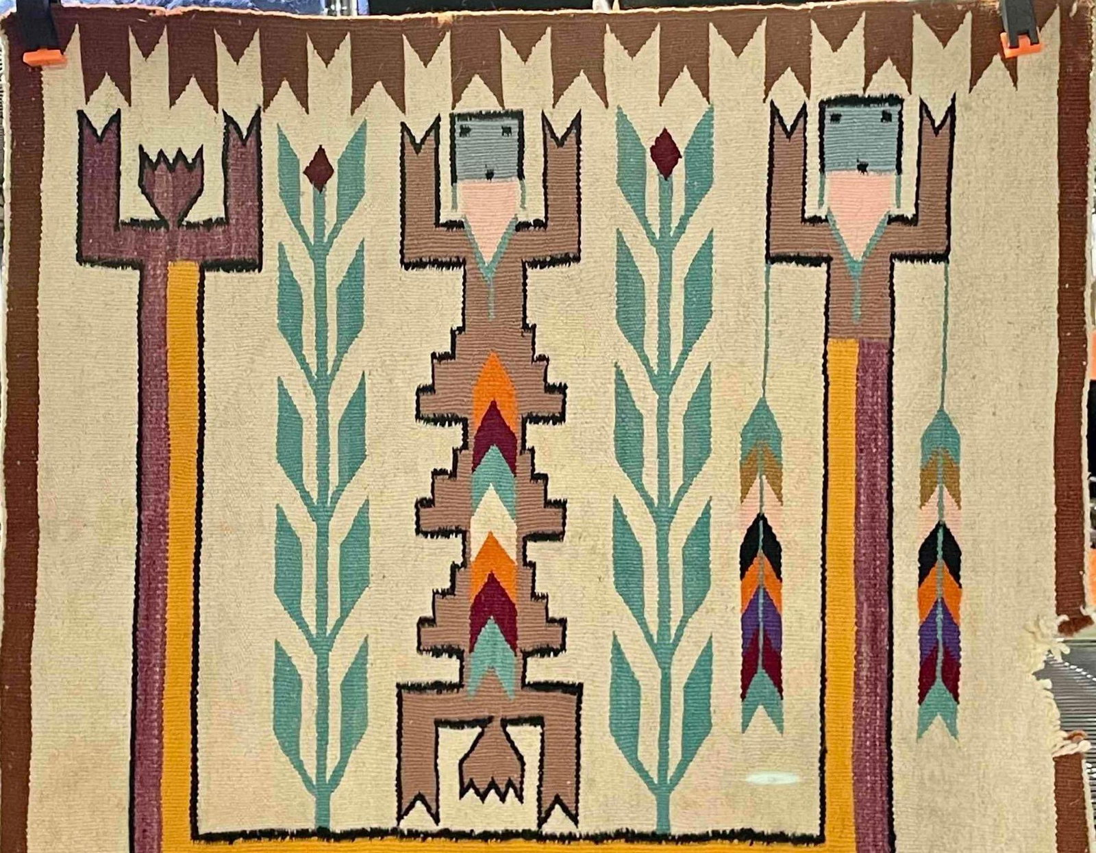Navajo Yei Woven Rug: Navajo Yei woven rug with three woven dancers and folliate/corn design within a brown border. Colors include brown, purple, orange, green, black, and red. Rug is in good condition but has a tear in lo