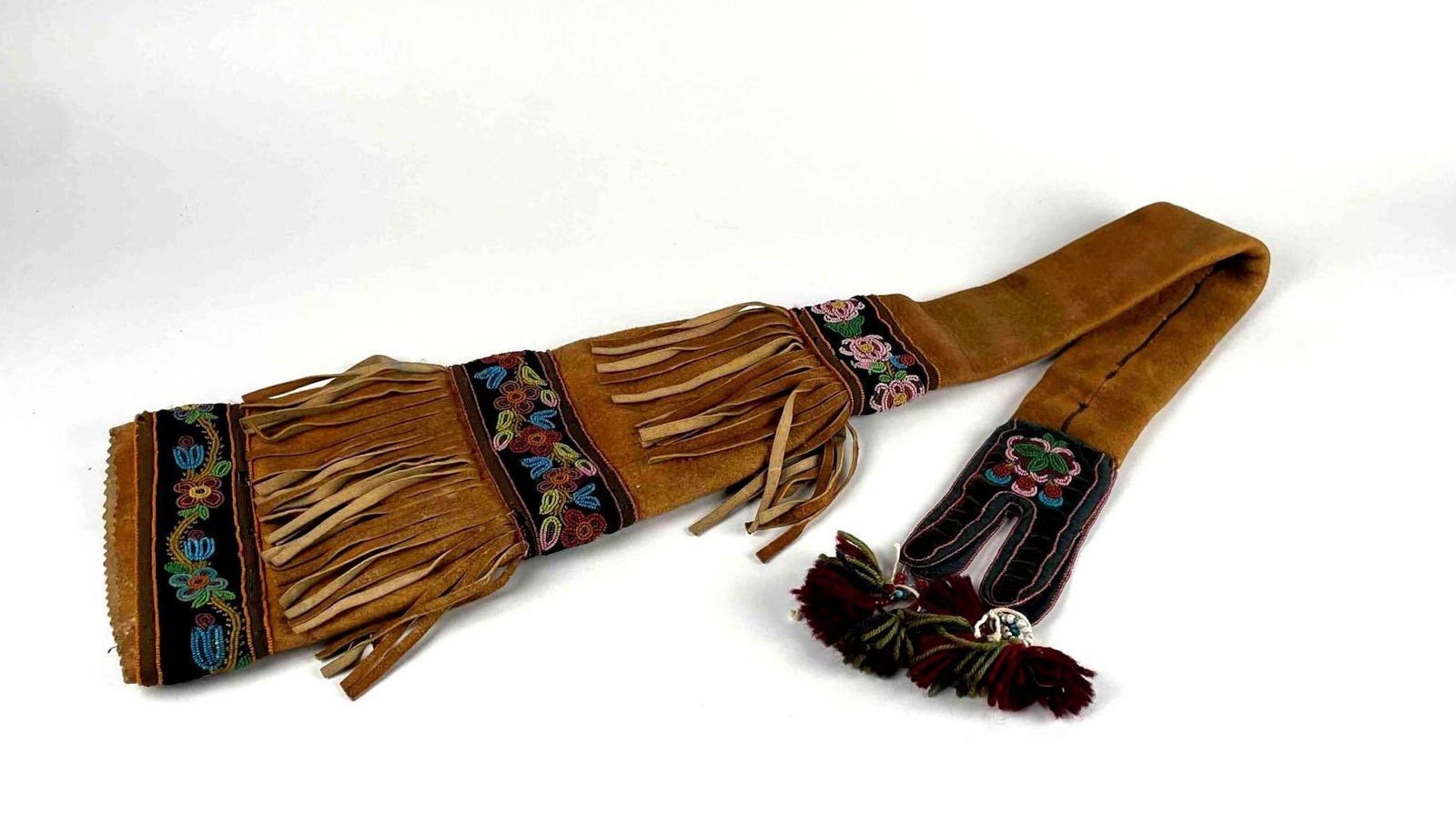 Athabascan Beaded Hide Rifle Case: An Athabascan beaded hide rifle case. Leather case with layers of fringe and velvet panels decorated with multicolor beaded floral detailing. Wool tassels hang off an end. Leather is in good condition