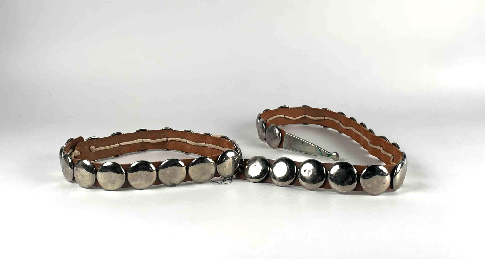 Native American Concho Strap: This item is a leather strap adorned with smooth, domed metal conchos, resembling elements of a concho belt but shaped like a leash or harness strap. The conchos are evenly spaced along the length of 