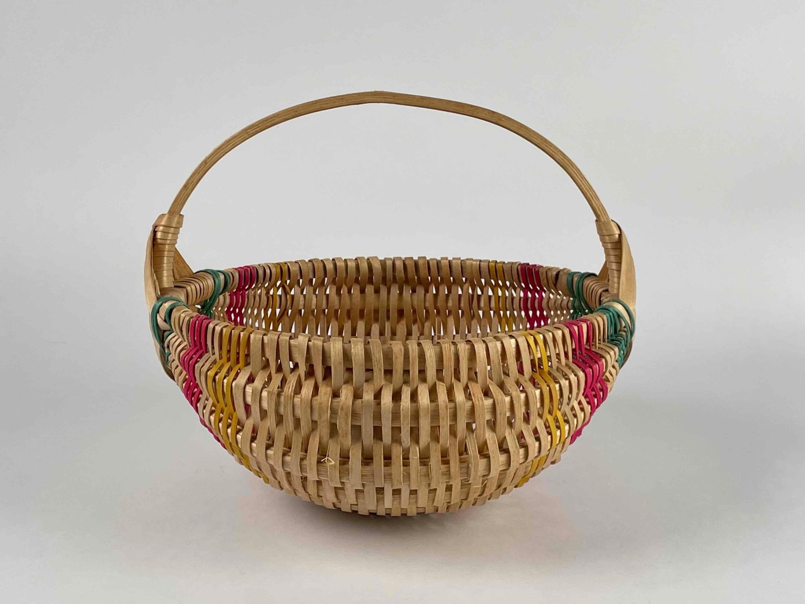 Southeastern Native American Handwoven Basket: Southeastern Native American handwoven basket with curved design. Basket has vibrant colored accents of pink, yellow, and green. Bent wood handle. Marked "25" on side of handle. In excellent condition
