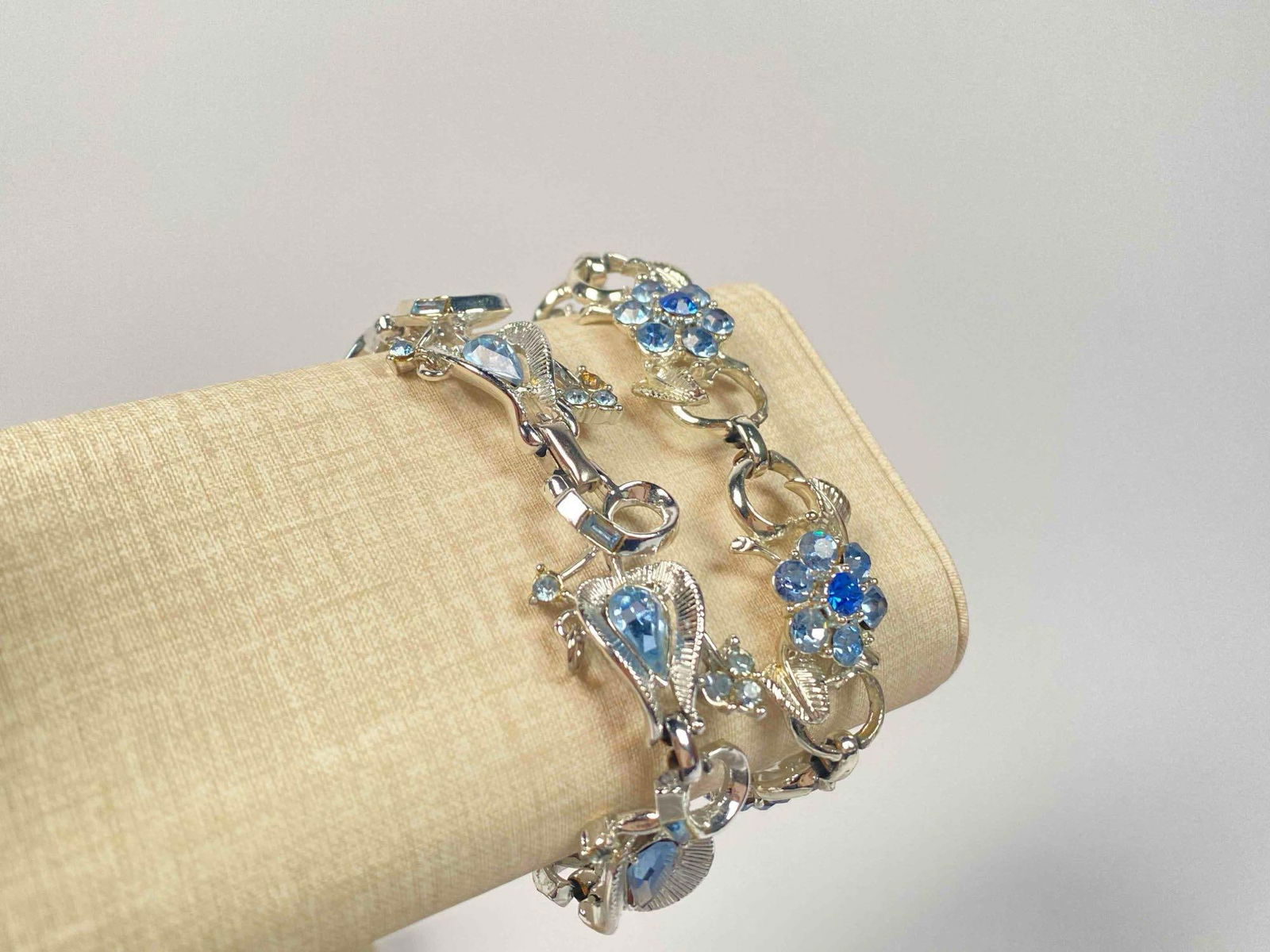 Pair of Coro Rhinestone Bracelets: Pair of Coro rhinestone bracelets. Bracelets have silver toned bands with ornate designs and blue toned rhinestones. One bracelet has floral design and round cut rhinestones, while the other has teard