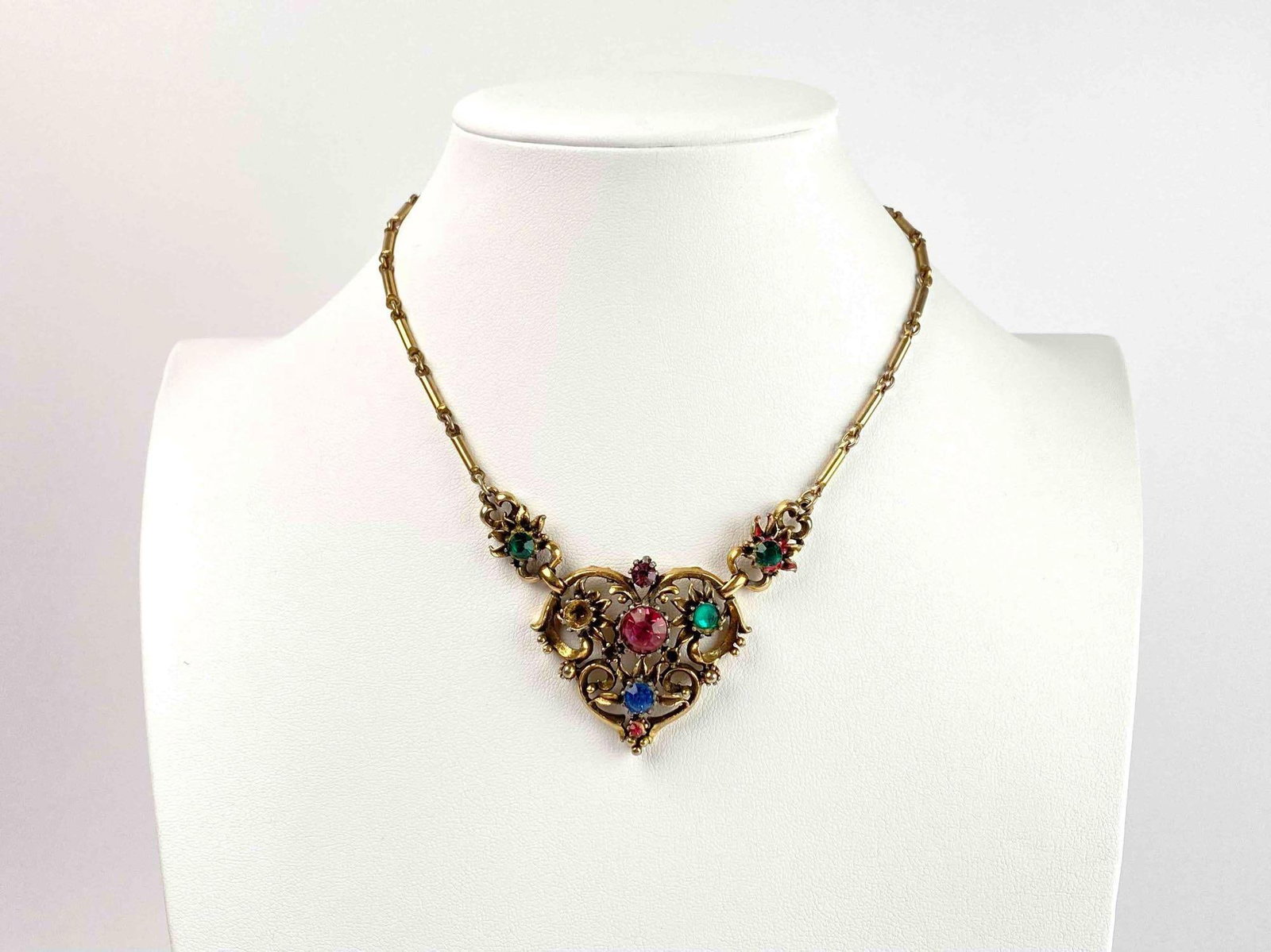 Vintage Coro Rhinestone Heart Shaped Pendant Necklace: Vintage necklace by Coro. Necklace has gold toned hardware and a heart shaped pendant decorated with multicolor rhinestones. Missing one rhinestone. Coro hallmark is decorated on back. In good conditi