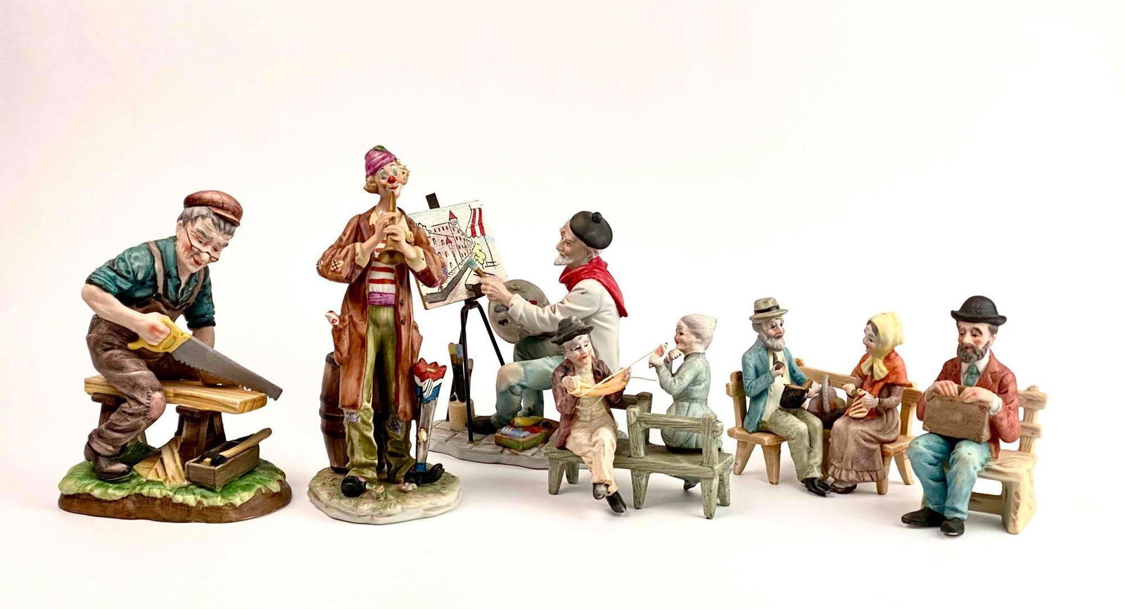Group of Porcelain Figurines (Lefton, Japan): Group of 6 figurines. Hallmarks labeled as Lefton and Made in Japan. Includes variety of sizes and designs such as people sitting on benches, a carpenter, a clown, and an artist. Hallmarks present on 