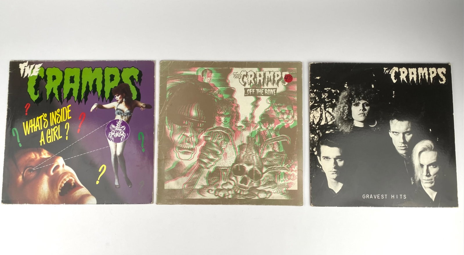 Collection of Three The Cramps Vinyl Records: Set of three vinyl records by The Cramps. Includes ‘Gravest Hits’ released by Illegal Records SP-501A, featuring tracks like ‘Human Fly’. ‘Off the Bone’, another release from Illegal Recor