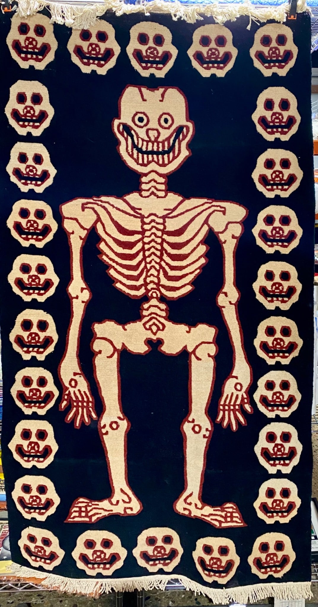 Three Tibetan Wool Hanging Rugs Featuring Skeleton and Skull Motif: Lot of three handwoven hanging rugs made from 100% wool, displaying a central skeleton motif surrounded by skull designs. One large rug and two smaller pieces. The pieces showcases intricate patterns 