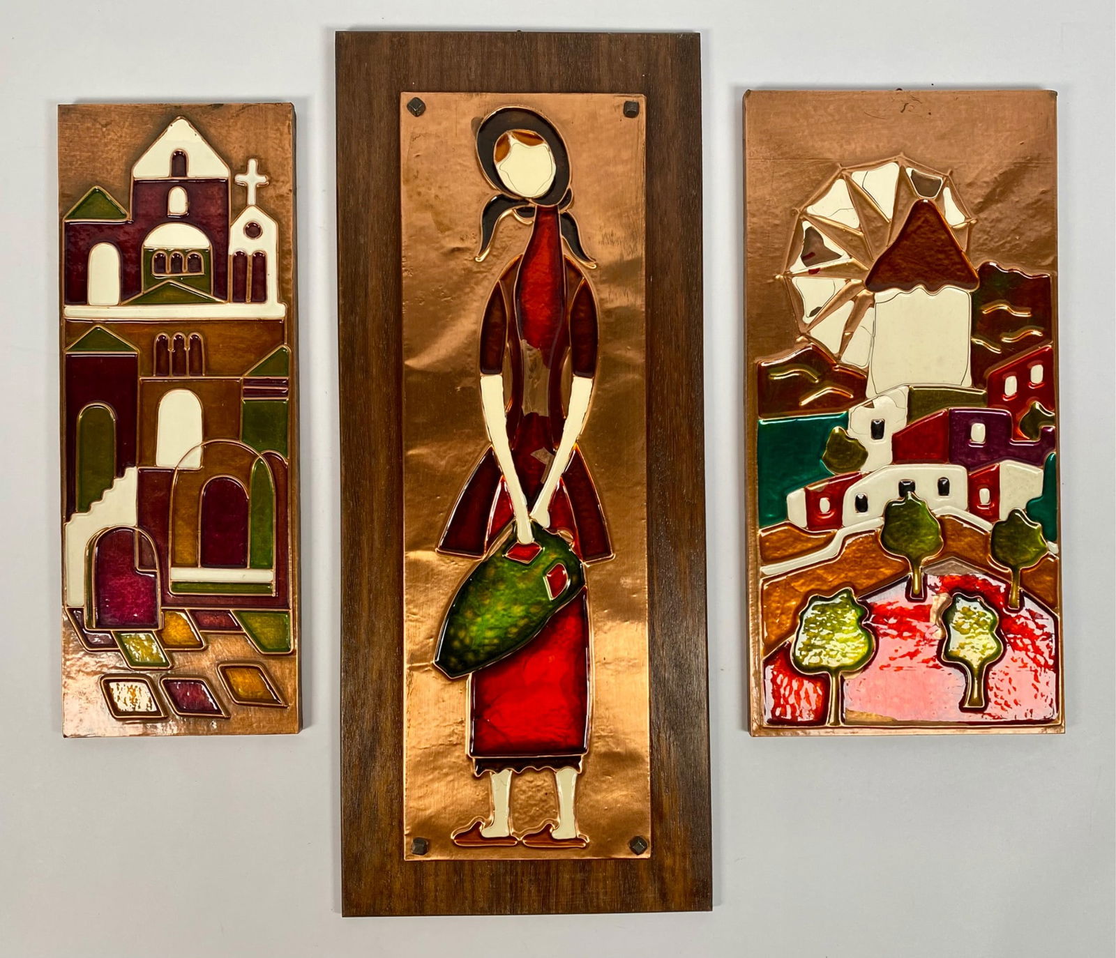 Set Of Three Greek Copper Enamel Wall Art: Set of three hand-crafted and hand-painted copper enamel wall art pieces, made in Greece. Includes depictions of a woman, a church, and a village scene with a windmill. Enamel colors include green, re