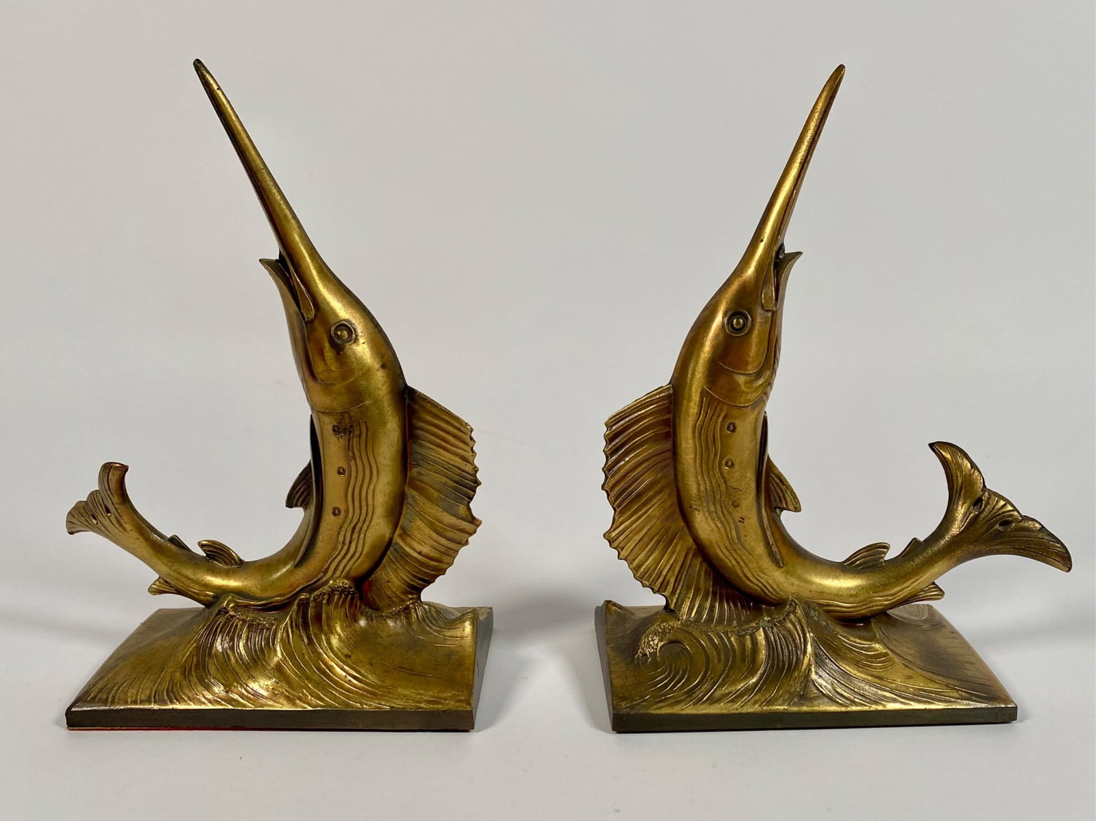 Pair of Marlin Brass Bookends by Philadelphia Manufacturing Co.: Set of two brass bookends designed as marlins on wavy bases. A label on the underside reads, â€˜A product of the finest American Craftsmanship, Philadelphia Mfg. Co., Philadelphia, PA.