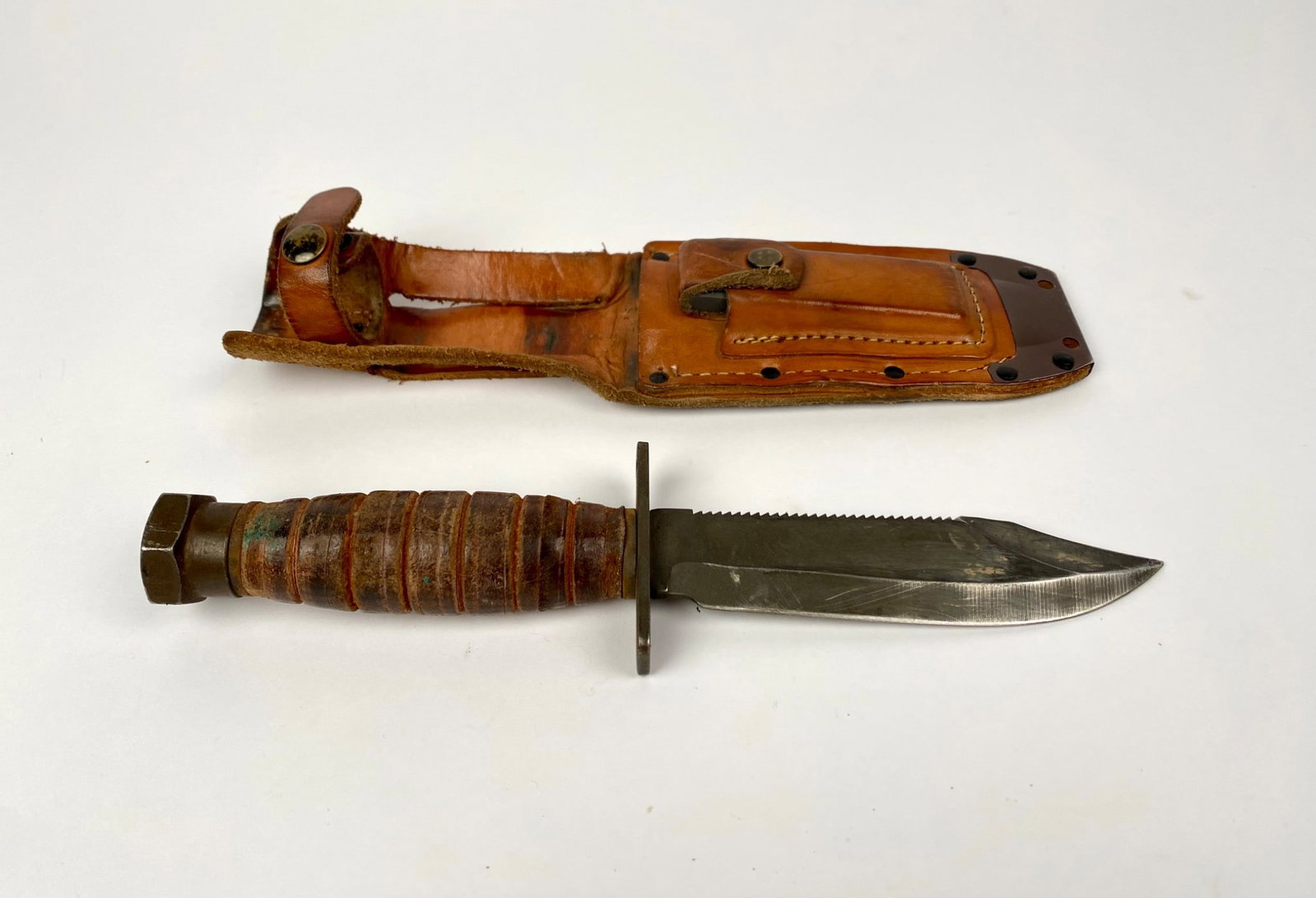 Ontario 9-87 Survival Pilot Knife with Sheath: Ontario 9-87 survival pilot knife featuring a 5-inch blade with a serrated back edge and leather washer handle. The knife includes a durable leather sheath with rivets and belt loop. Makerâ€