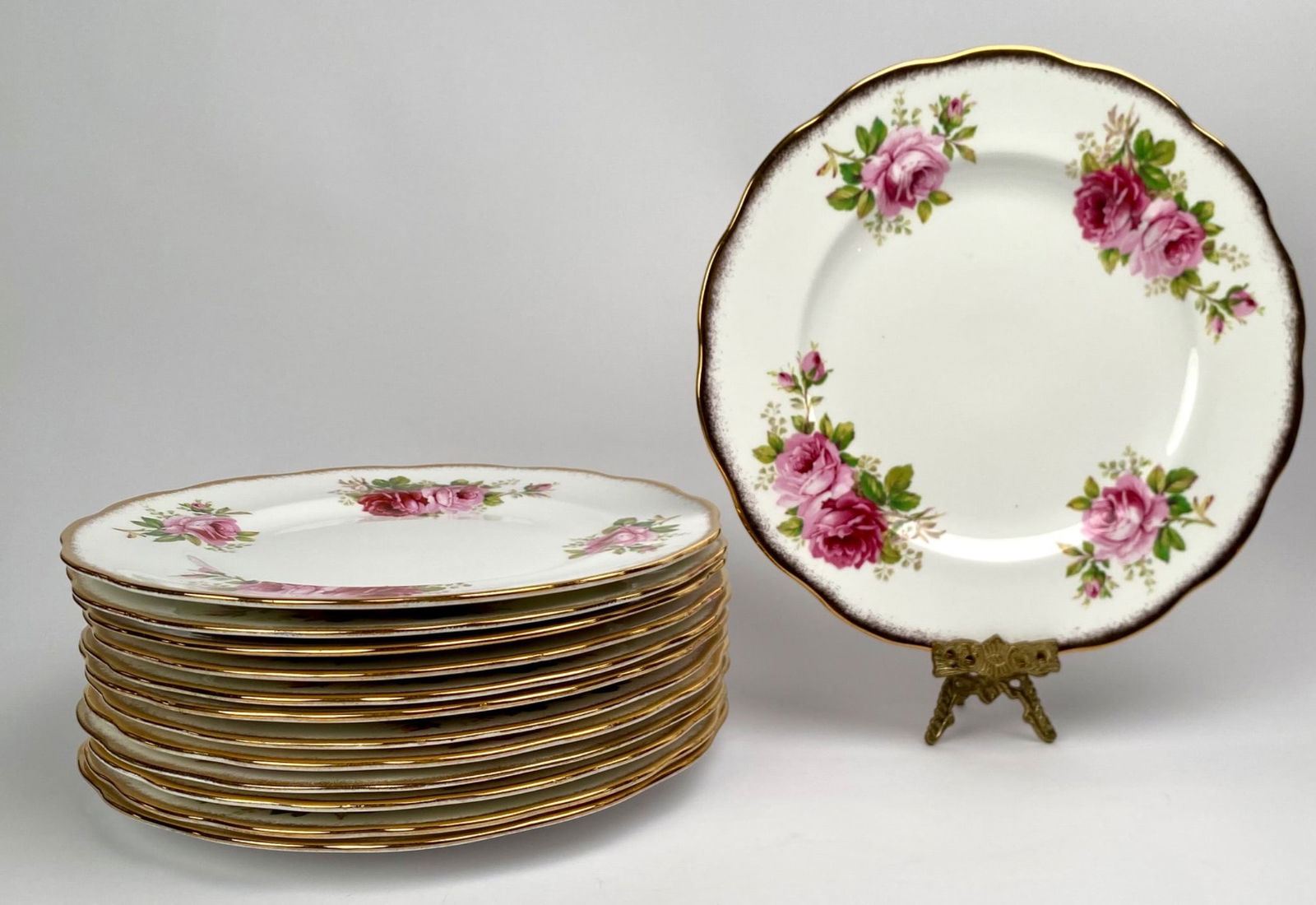 13 Royal Albert American Beauty Dinner Plates with Pink Roses and Gilded Edges: Set of 13 Royal Albert â€˜American Beautyâ€™ dinner plates featuring detailed pink rose patterns and scalloped edges adorned with gold trim. These porcelain plates sho
