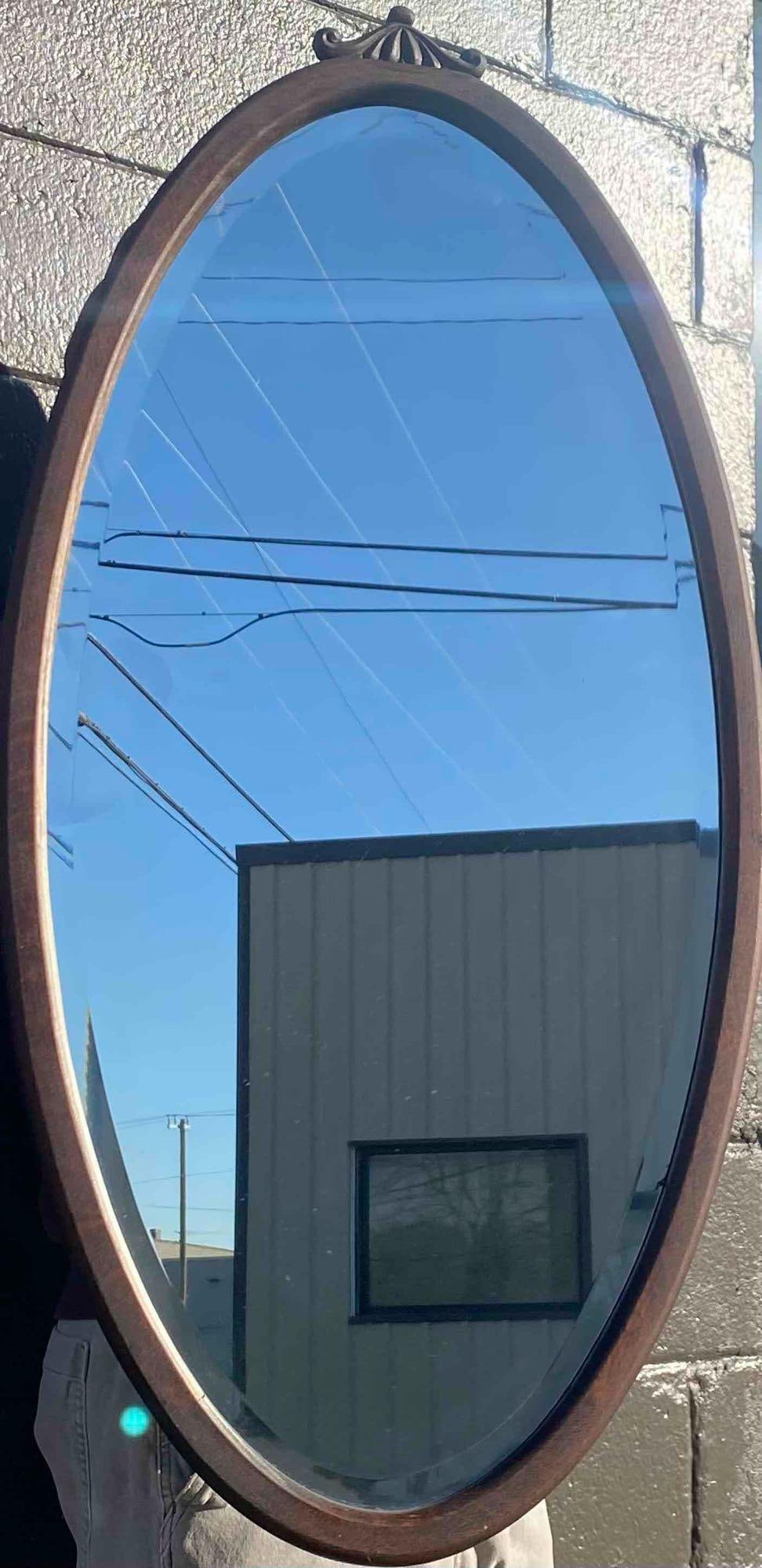 Oval Wooden Framed Wall Mirror with Scroll Top Accent: Oval-shaped mirror featuring a wooden frame with a decorative scroll accent at the top. The frame has a warm-toned finish and shows visible wear and age-appropriate markings. The back panel shows sign