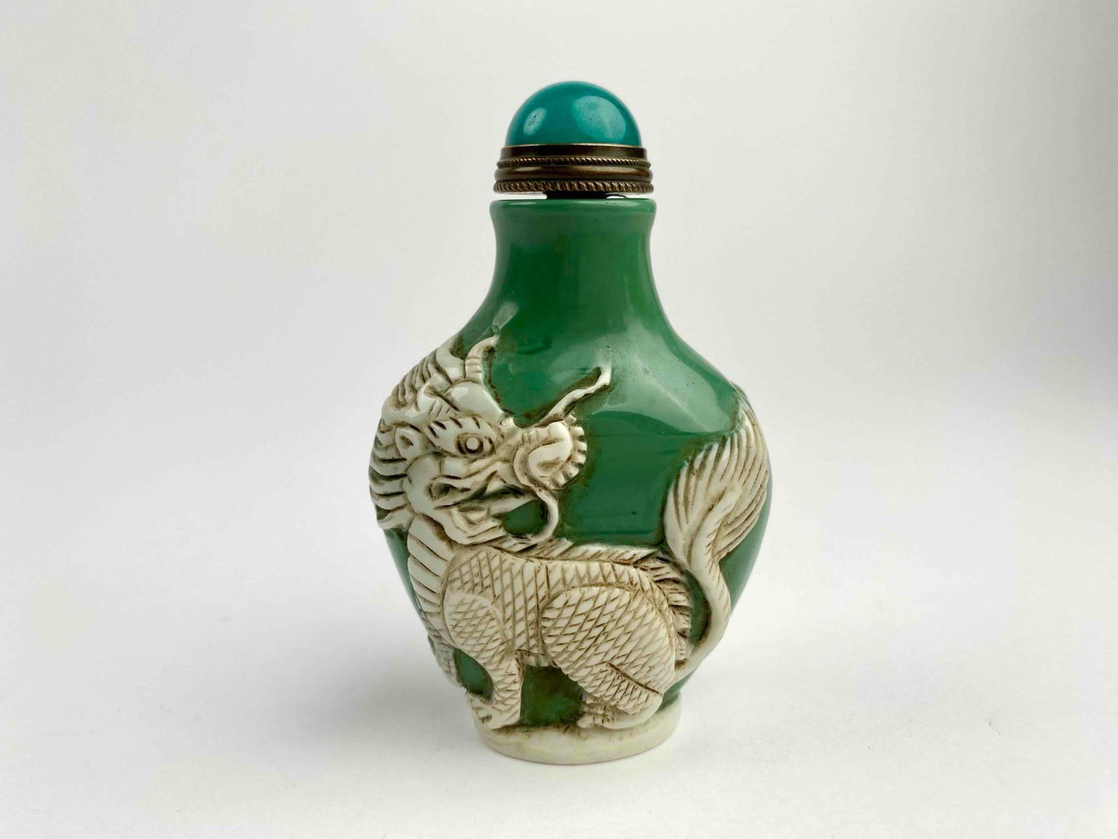 Green Porcelain Snuff Bottle With Dragon and Elephant Relief: Chinese snuff bottle with overlay. Snuff bottle is green with white overlay and a turquoise style cap. Bottle and scoop are in good condition. Please see photos for additional details. | Dimensions: 2