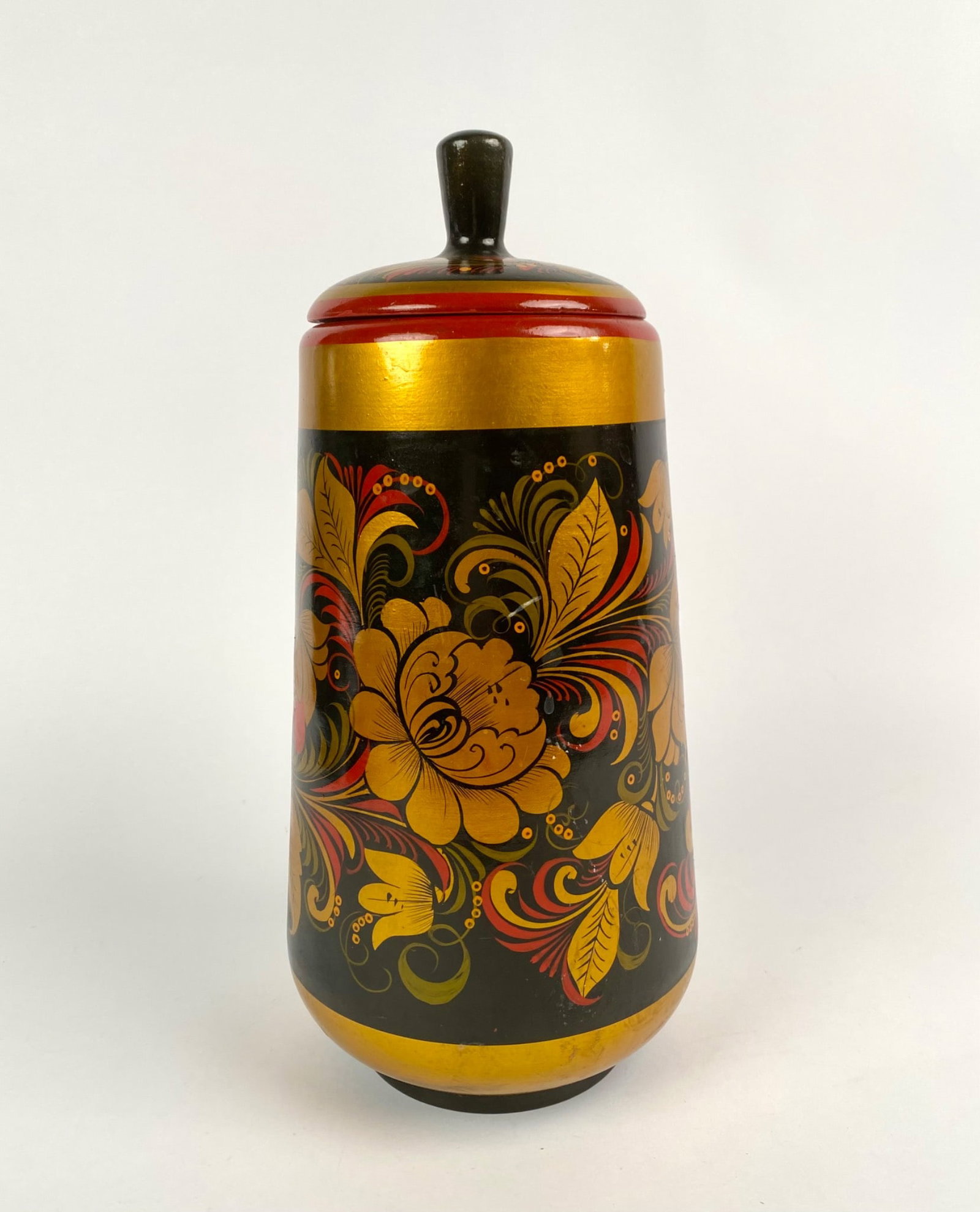 Russian Khokhloma Lidded Wooden Vessel With Hand-Painted Floral Design in Red, Black, and Gold: Lidded wooden vessel featuring a hand-painted floral design in red, black, and gold with additional green highlights. The container is cylindrical, tapering slightly towards the lid, which includes a 