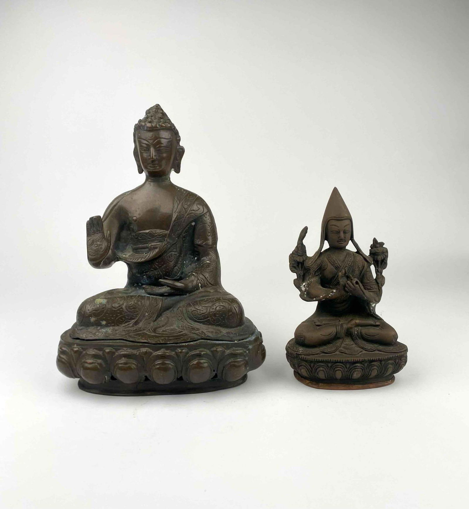 Pair of Antique Bronze Buddhist Figures on Lotus Bases: A lot of two bronze Buddhist figures. The first is an intricately designed statue of the Buddha in a seated meditative pose, adorned with detailed robes and resting on a lotus base. The second is a Bu
