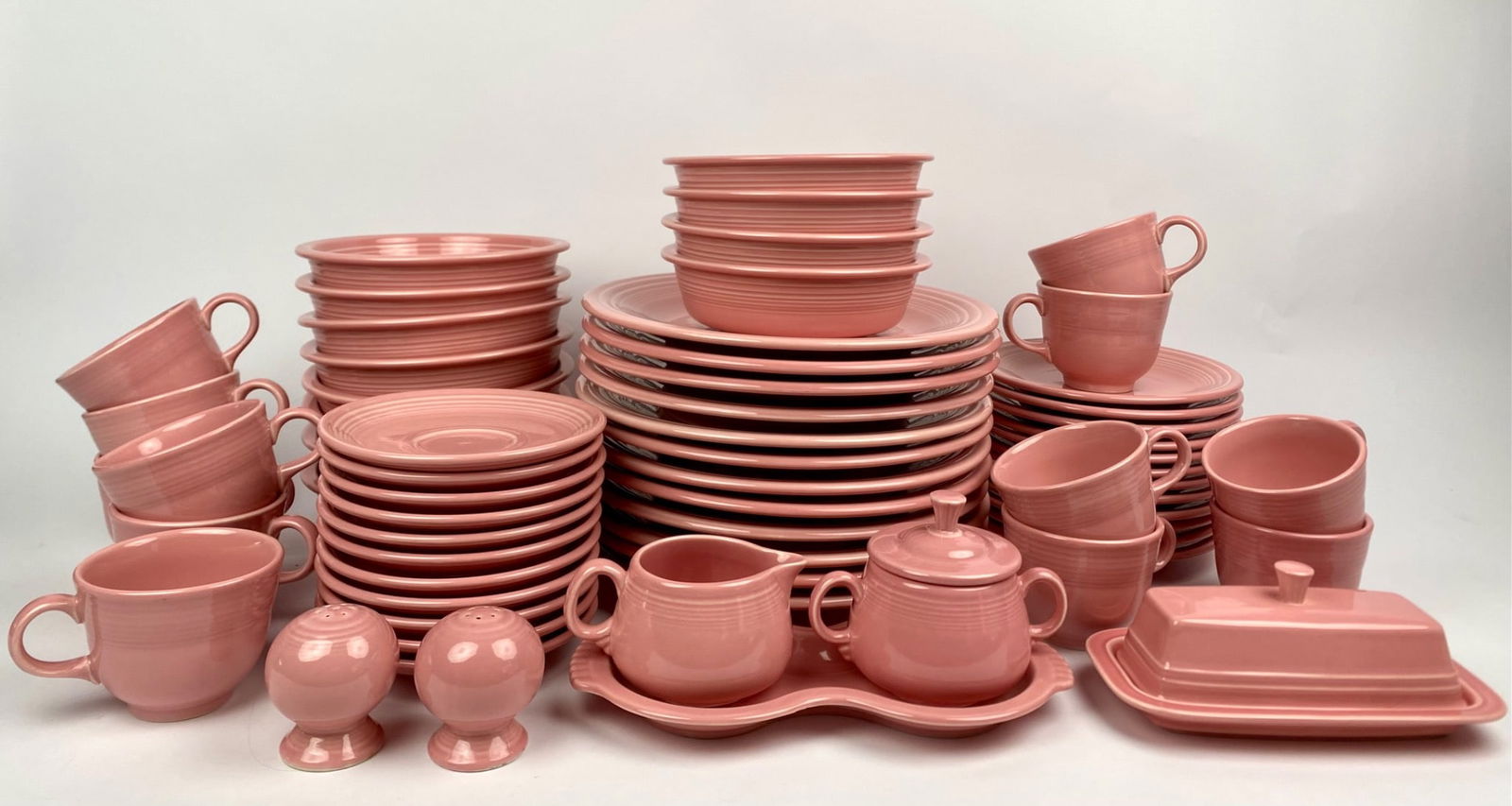 Large Lot of Fiesta Pink Dinnerware (Plates, Bowls, Cups, and Accessories): A large collection of Fiesta dinnerware in pink glaze, featuring assorted matching items, including 12 dinner plates, 12 dessert plates, 12 cups with 11 saucers, 12 bowls, a covered butter dish, a pai