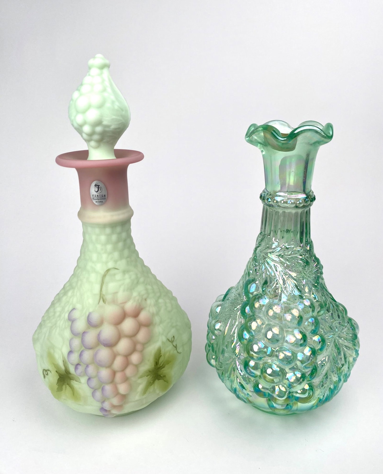 Fenton And Imperial Glass Decanters: Two decorative cruets, one by Fenton and one by Imperial Glass. The Fenton piece, handcrafted in the USA, is made of milk glass with a textured grape motif and handpainted details. It includes a match