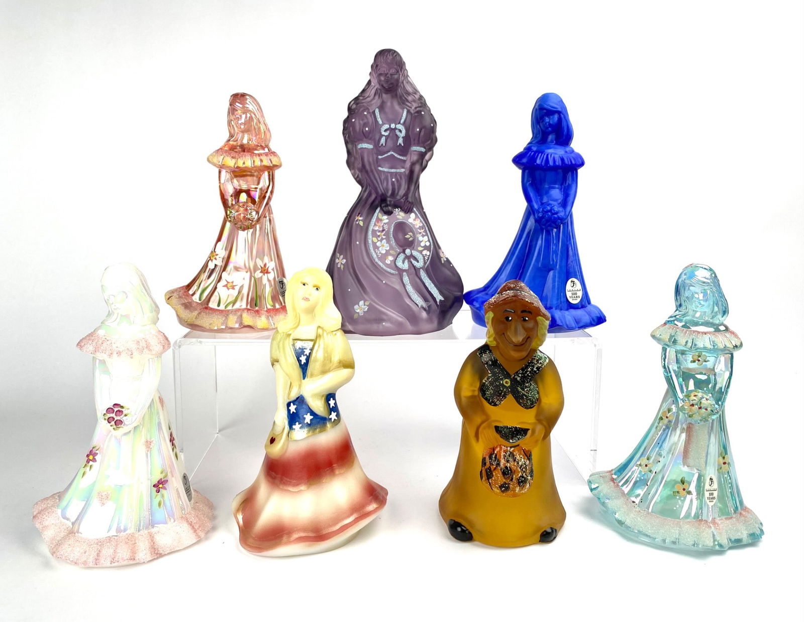Seven Fenton Glass Figurines: Set of seven glass figurines depicting women in various styles and colors. The pieces are intricately hand-painted with floral and themed designs. Each figurine includes markings or artist signatures