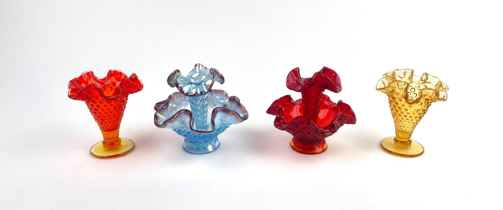 Four Fenton Glass Epergnes Vases: Set of four Fenton glass miniature horn vases in vibrant colors, including orange, light blue, red, and amber. Each vase features a ruffled top design and finely detailed hobnail or diamond patterns.