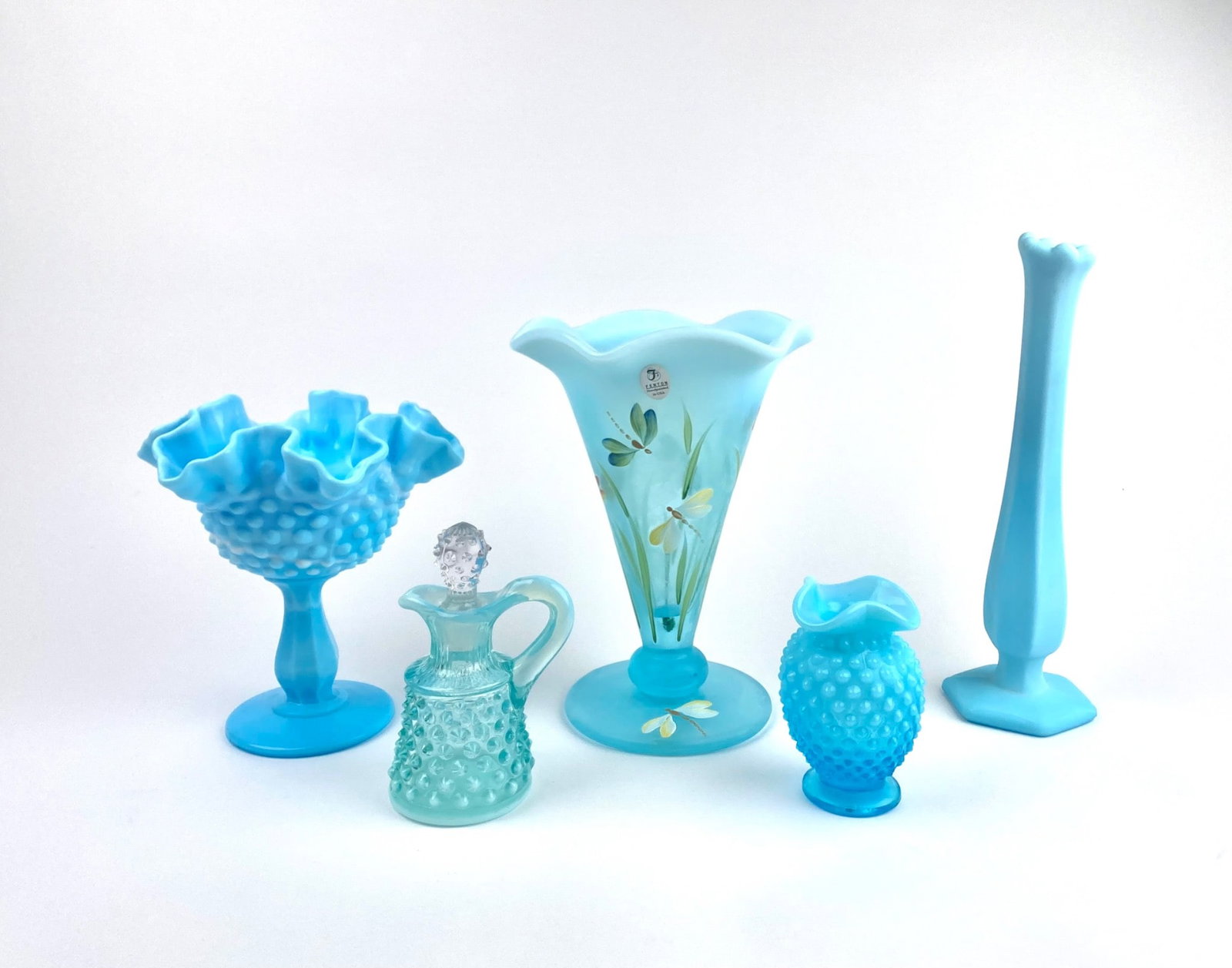 Lot of 5 Blue Fenton Glass Vessels: Lot featuring five stunning light blue glass pieces, including an intricately designed ruffled glass compote, a painted glass vase adorned with dragonfly and floral motifs, a tall slender vase, a hobn