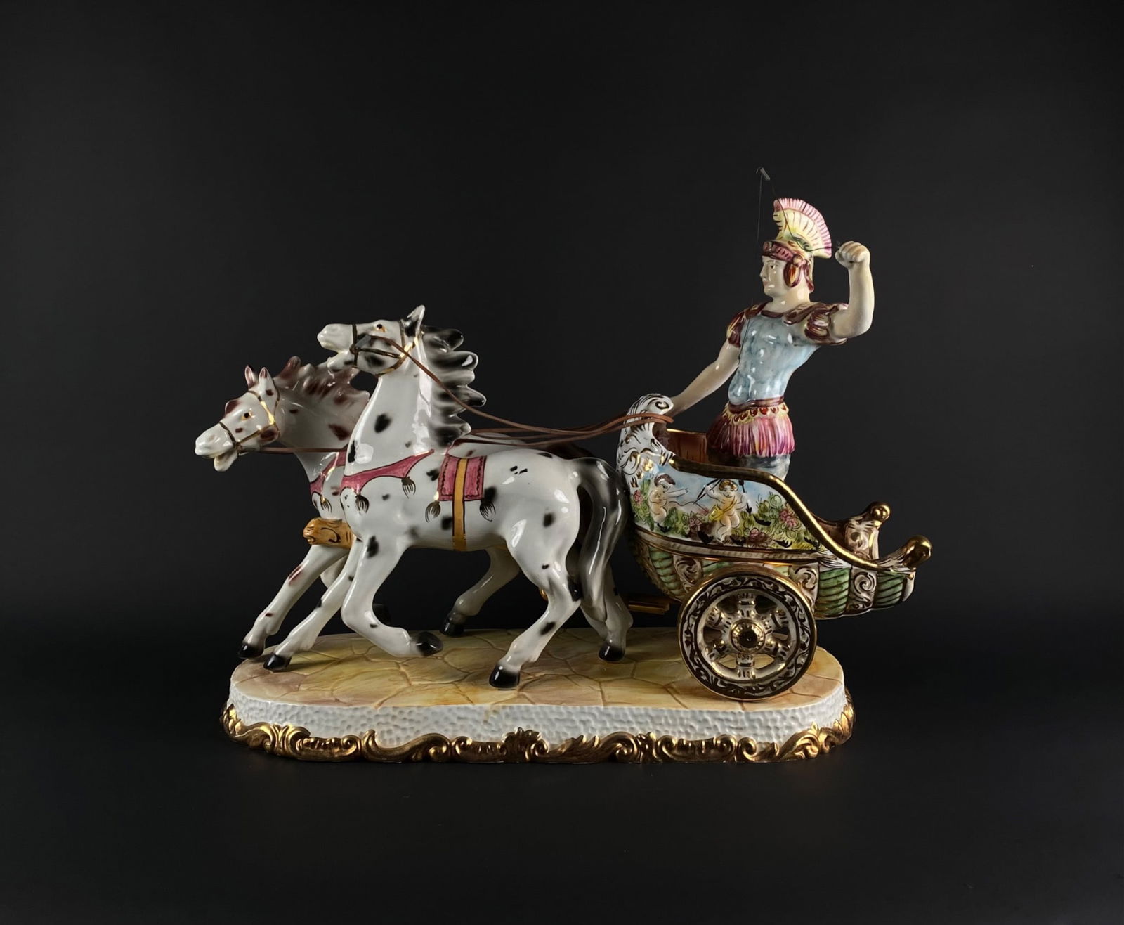 Capodimonte Chariot Figurine With Rider and Horses: Hand-painted porcelain figurine depicting a rider in Roman-style armor on a decorative chariot pulled by two horses. Features intricate gold and colored accents, as well as relief and painted designs