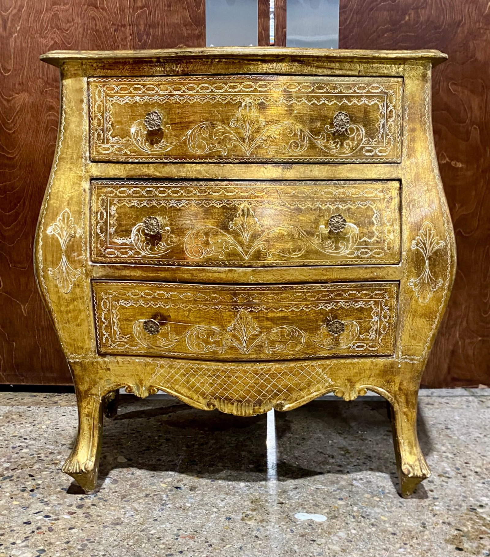 Gold-Gilded Wooden 3-Drawer Bombe Chest with Intricate Carving: Gold-gilded wooden bombe-style chest featuring three drawers with floral and scroll detailing on the front, sides, and top. Each drawer is accented with ornate floral metal knobs. The piece exhibits a