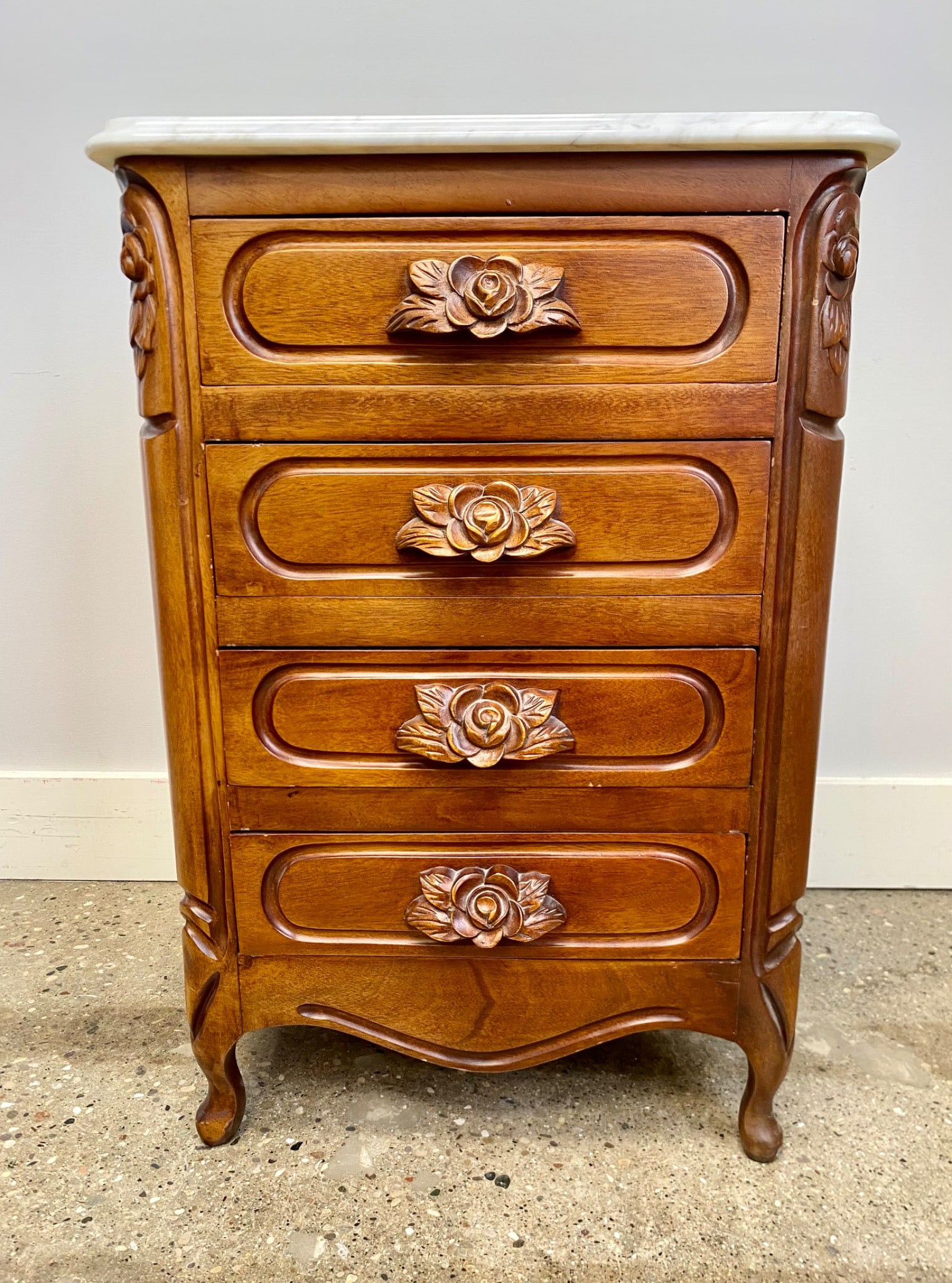 Wooden Chest of Drawers with Floral Motifs and Marble Top: Wooden chest of drawers with four pull-out drawers featuring intricate carved floral motifs on the fronts. The piece has curved legs, a beveled wood build, and a removable white marble top with rounde