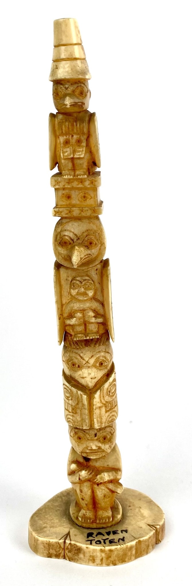 Carved Bone Raven Totem with Indigenous-Inspired Design: A detailed carved bone sculpture of a Raven Totem featuring an Indigenous-inspired design. The totem is crafted with multiple symbolic figures including a raven and other intricate representations. Th